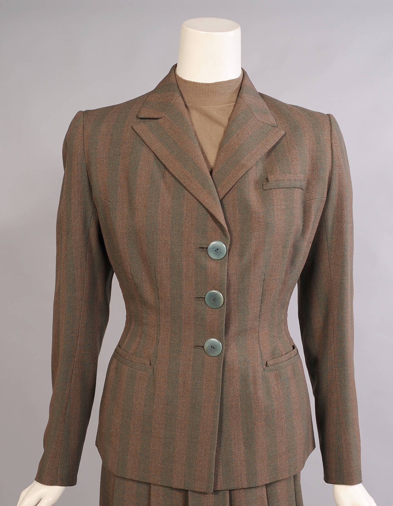 A rare and elegant example from the 1940's this Hermes striped wool suit has a classic blazer with a nipped in waist, a two tone sweater, and a long skirt with a pleated front. The jacket and skirt are made form a subtle green and brown striped