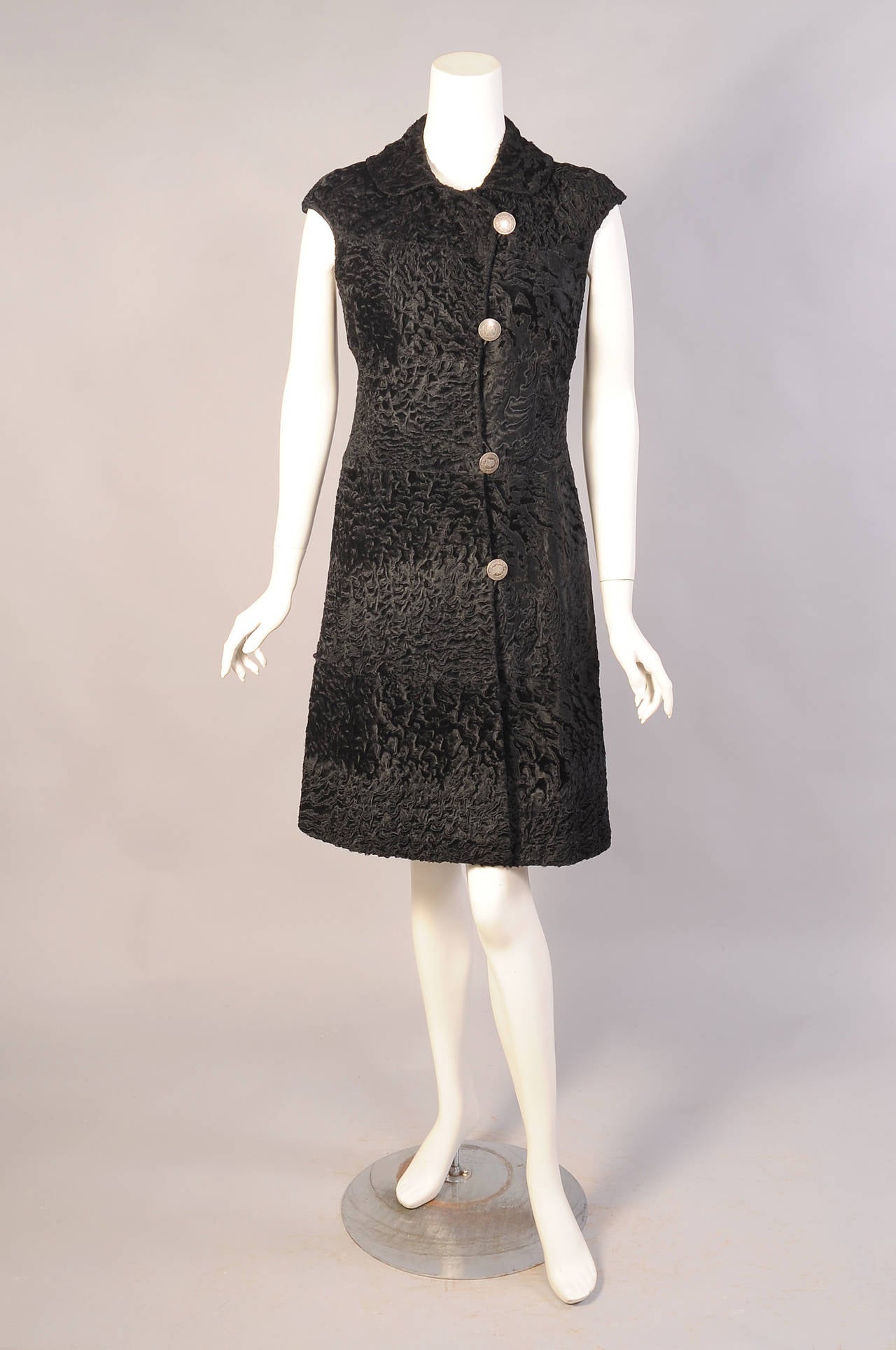 This sleek black Russian broadtail coat or dress is made from wide bands of fur. It has cap sleeves and a rounded collar. It closes left of center with large coin buttons. Retailed by lord & Taylor it is fully lined in black silk and it is in