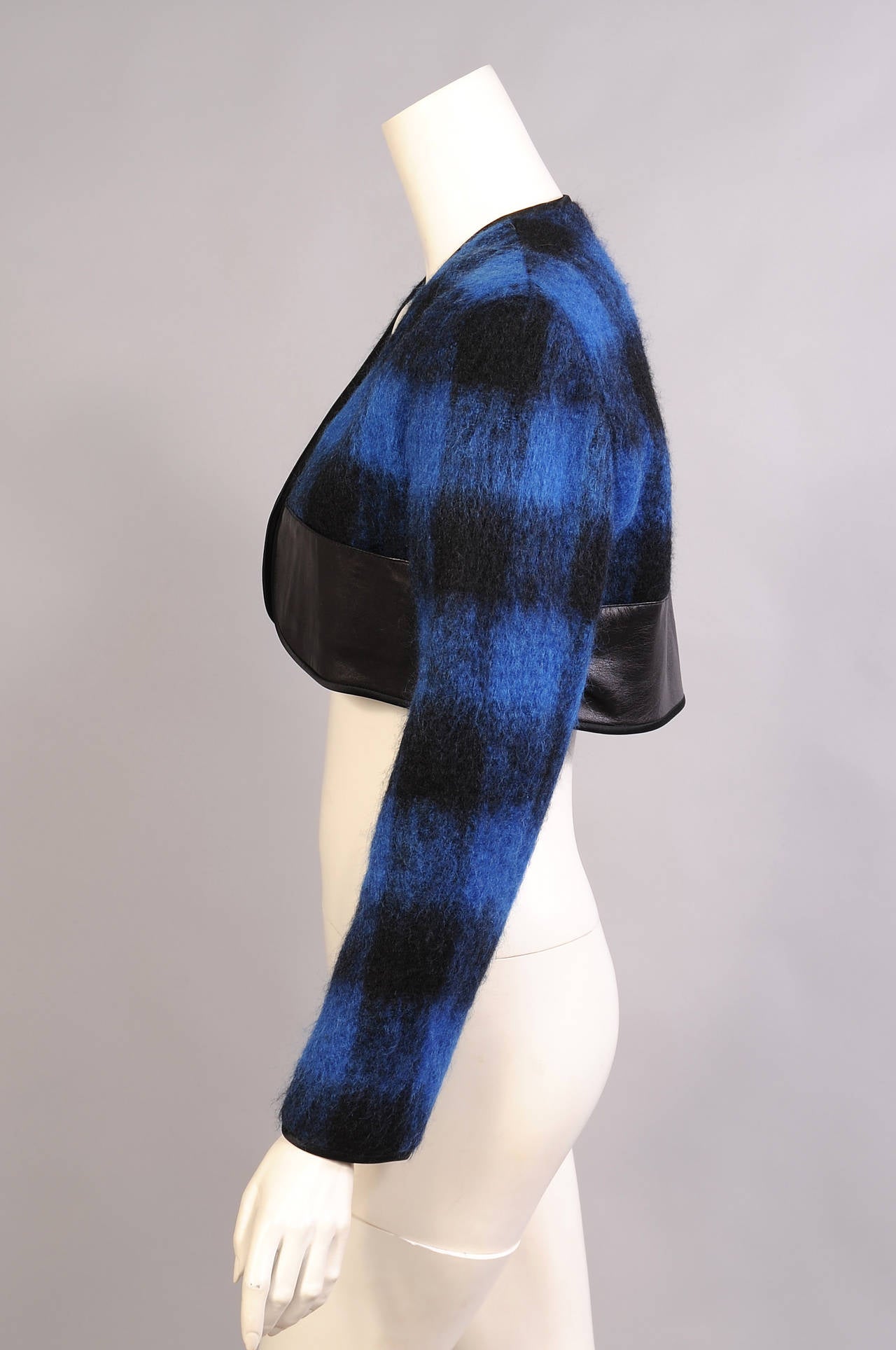 A bold black and blue mohair and wool plaid bolero has a wide band of black leather at the bottom. The jacket and cuffs are trimmed with black satin. It is fully lined in black silk and marked a size 6. It is in excellent