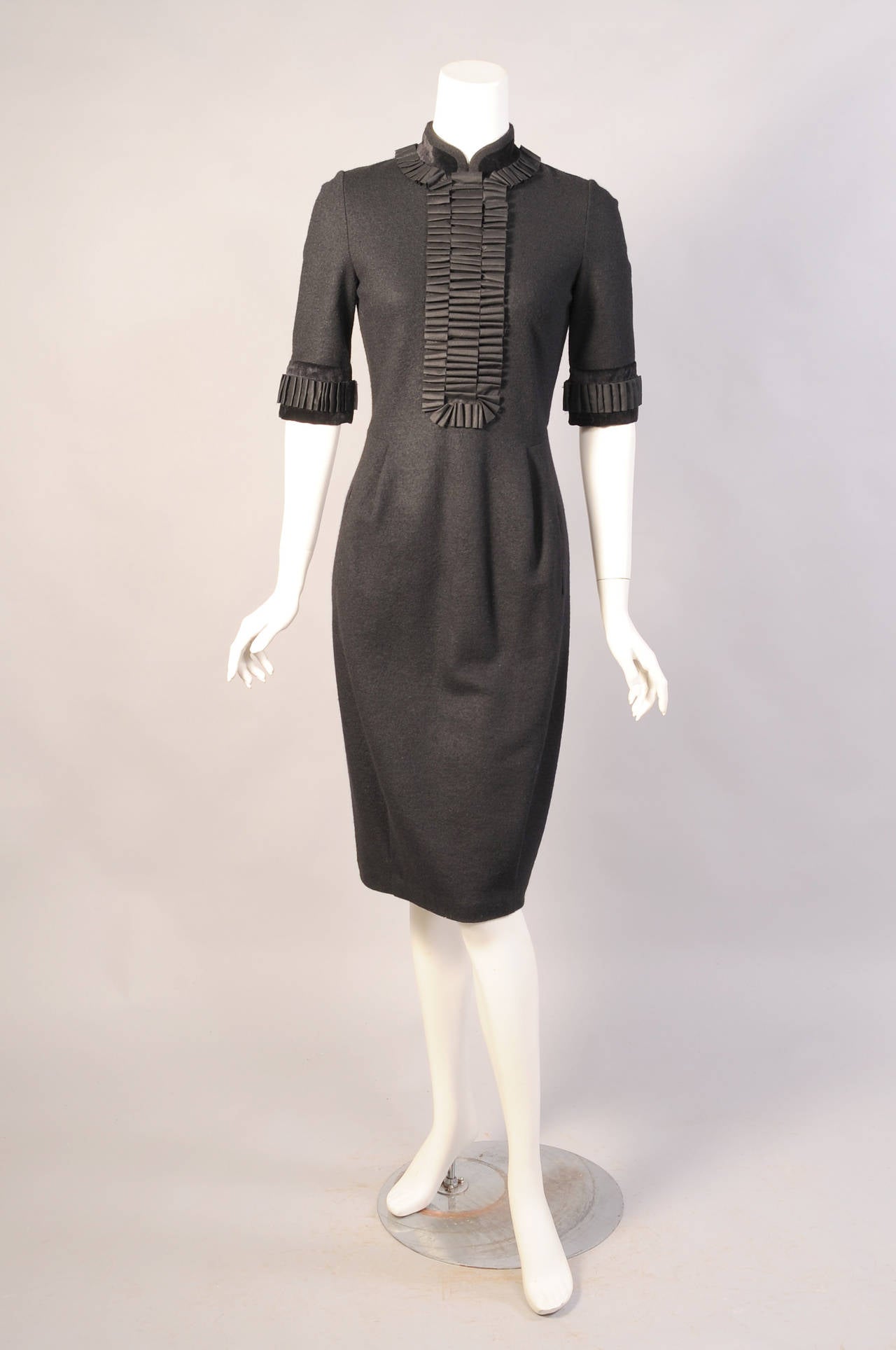 A black velvet collar and cuffs is trimmed with pleated black silk ribbon in the style of a tuxedo shirt. It elevates this black wool dress from Yves Saint Laurent to the next level. The dress has a nipped in waist, two velvet edged pockets and the