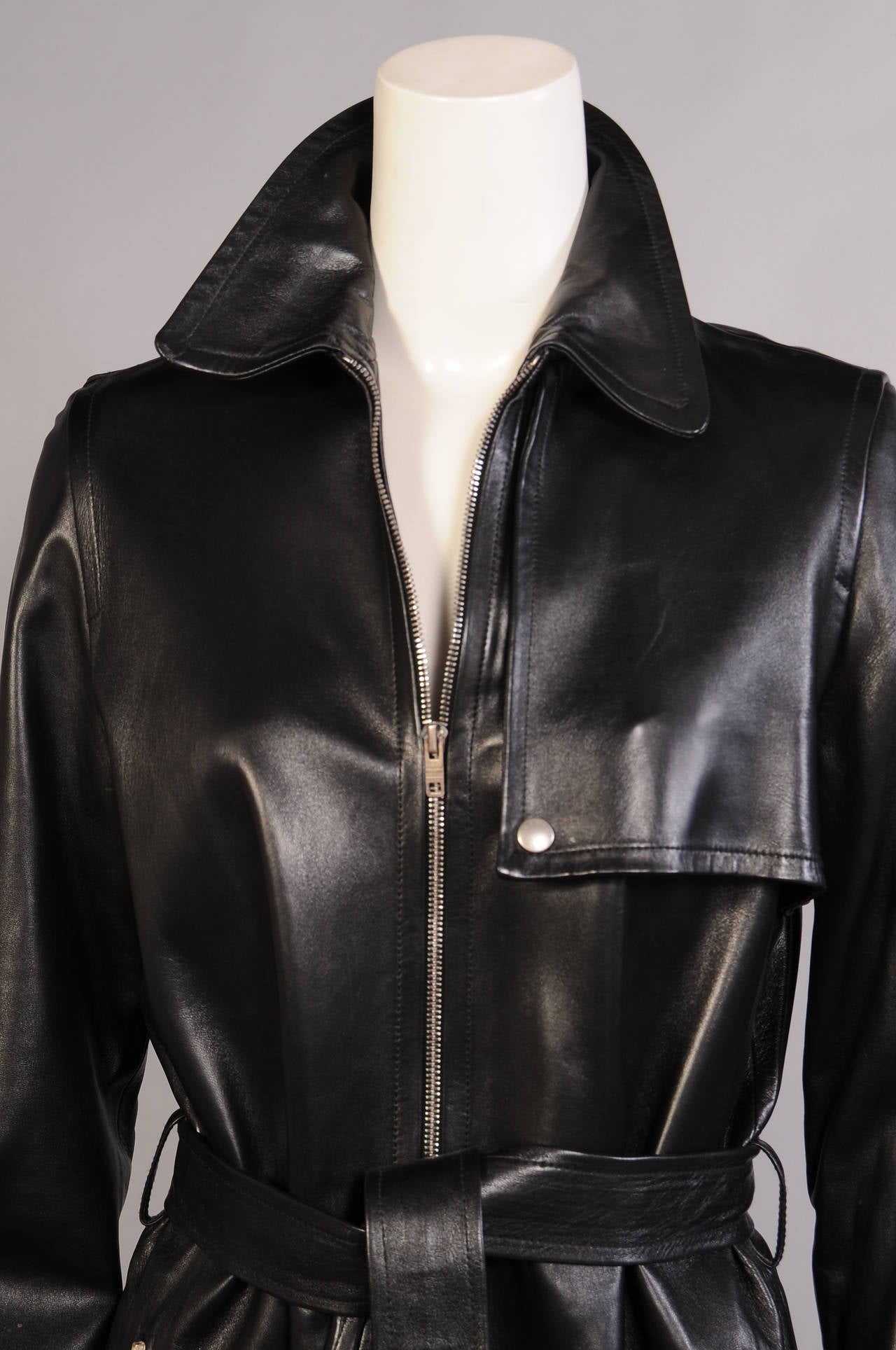 Light weight, butter soft black lambskin is accented with metal zippers on the pockets and the center font closure. The coat is cut in the classic belted trench coat style. It is marked a size 38 and it is in excellent