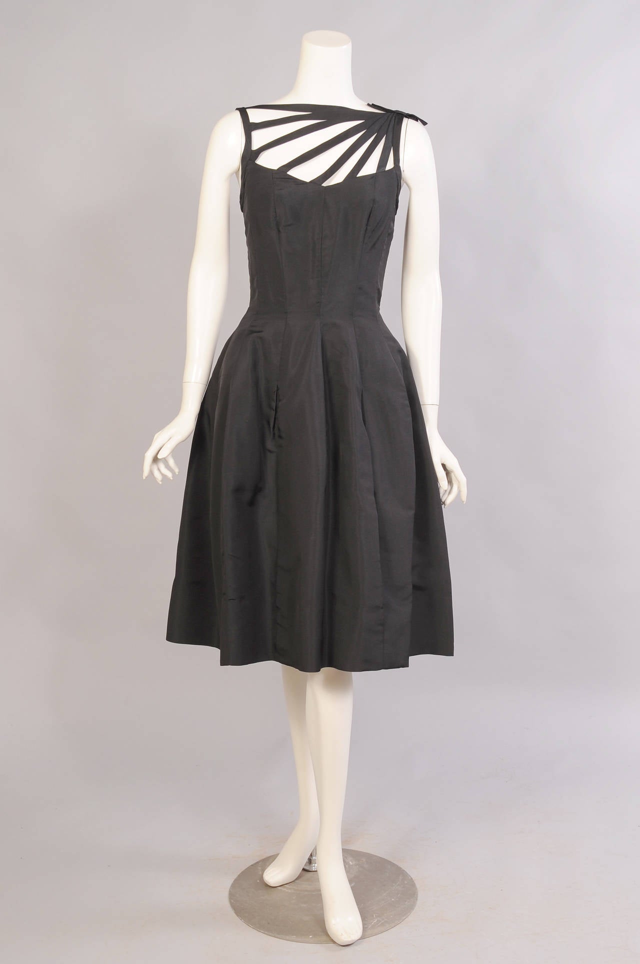 This chic black silk cocktail dress has a wonderful strappy treatment on the bodice with a flat bow on the left side. The bodice is boned for extra support. The full skirt has inverted pleats which create an interesting shape. There is a black net