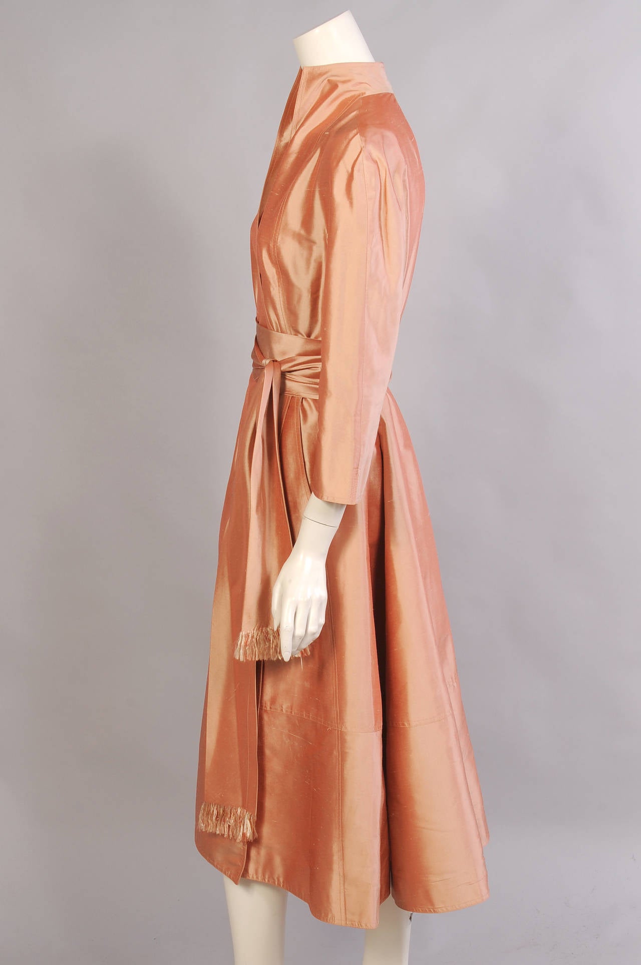 An iridescent silk in a sherbet shade of peach is used for this wrap dress from Ralph Rucci. The dress has a modern version of a Mandarin collar. There are ties inside and it hooks on the left side. There are two pockets hidden in rhe curving seams.