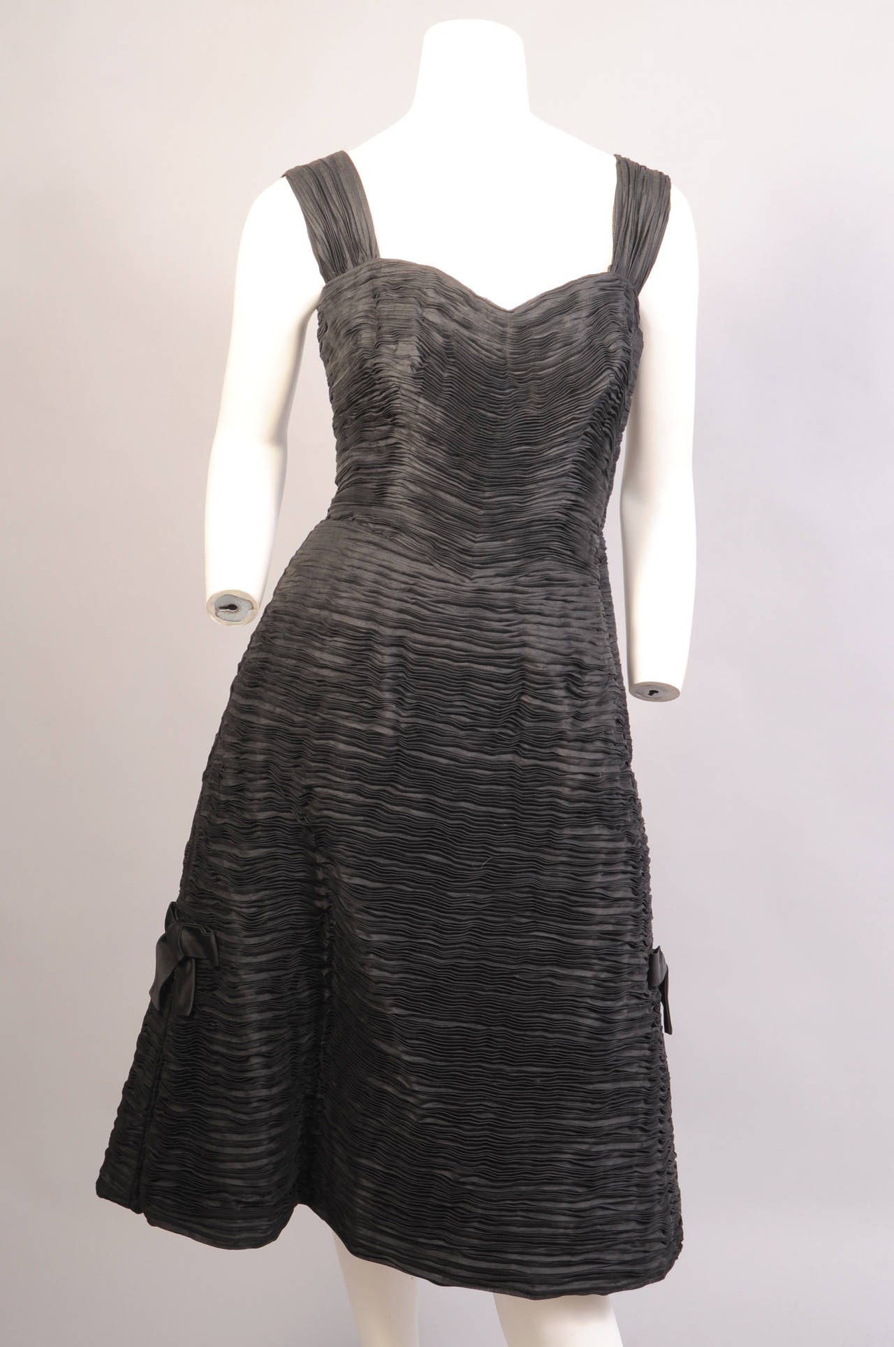 This inky black pleated linen dress is so elegant. The dress has wide straps , a sweetheart neckline with a boned bodice and a left side zipper above a full skirt. The skirt is trimmed with black silk bows on either side above an inverted pleat. The