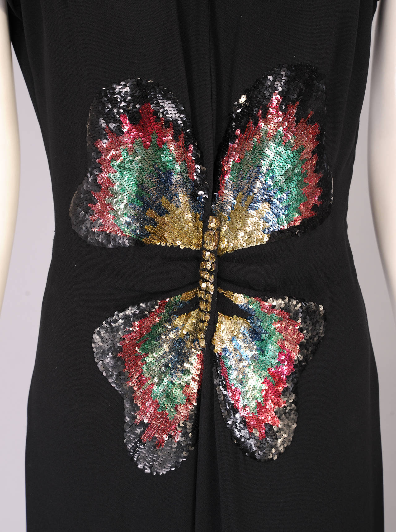 Classic and elegant, this 1940's evening gown has cap sleeves, a self tie at the neckline, a fitted waist above a long skirt with a center pleat. This is the backdrop for a spectacular multi color sequin butterfly with a three dimensional body