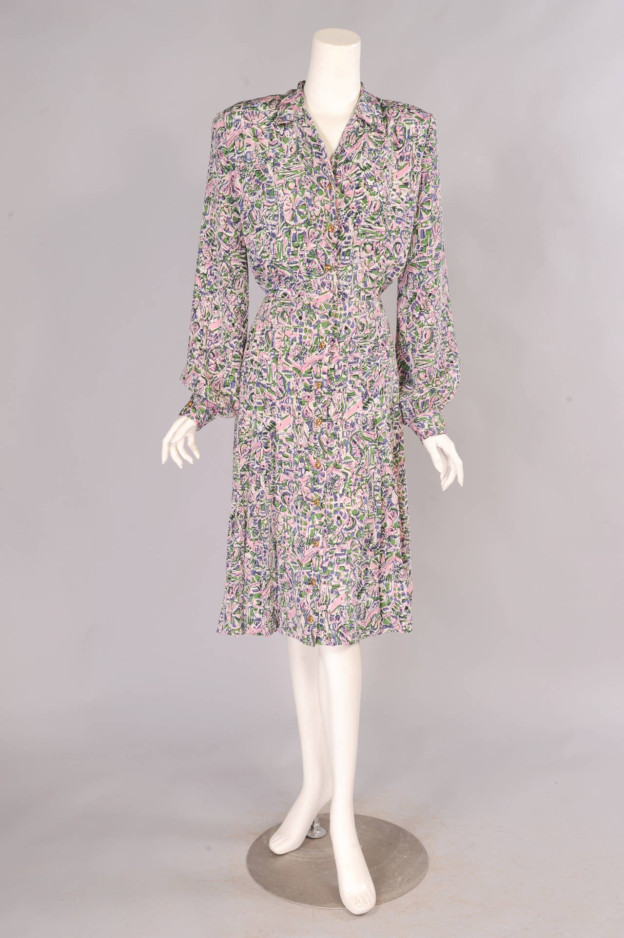 An abstract print in pink, green and lavender is used for this 1940's silk day dress. There is a row of gold toned buttons all the way down the front of the dress. The cuffs have matching buttons. The skirt has stitched down pleats over the hips and