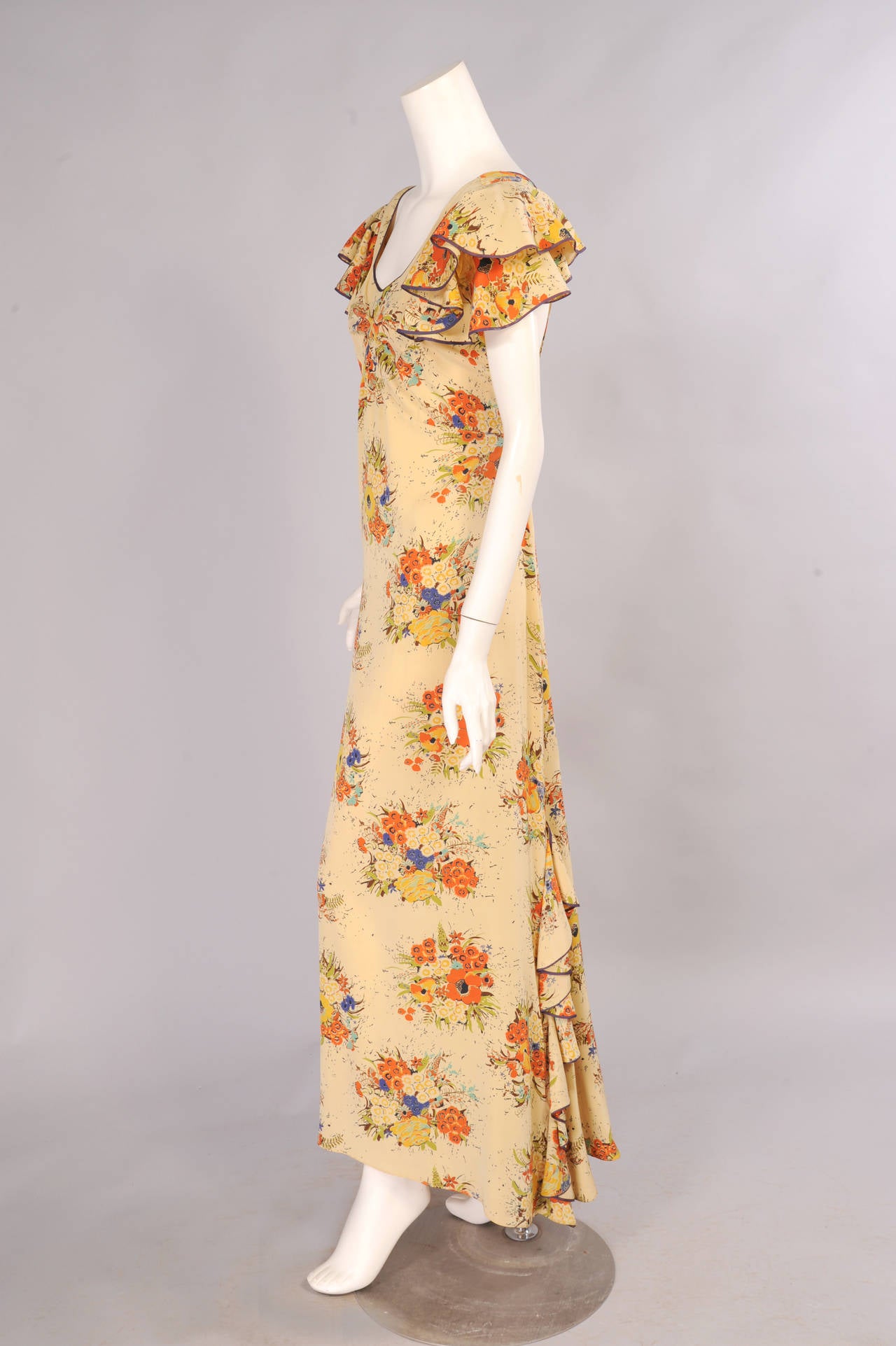A charming floral bouquet adds color to this pale butter yellow silk dress that is piped in navy blue at the neckline, on the sleeves and the flirty ruffles on the train. The dress has wide straps that criss cross in back above a snap closure. It is