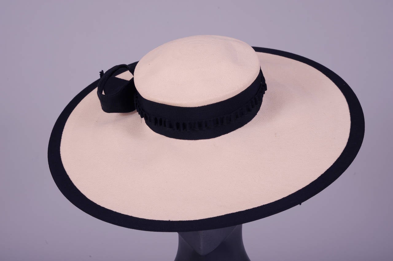 The finest hand woven natural Panama straw is combined with black grosgrain ribbon for this elegant wide brimmed hat from the 1930's. A wide ribbon hat bandis trimmed with a narrow gathered ribbon at the center. The edge of the brim is trimmed with