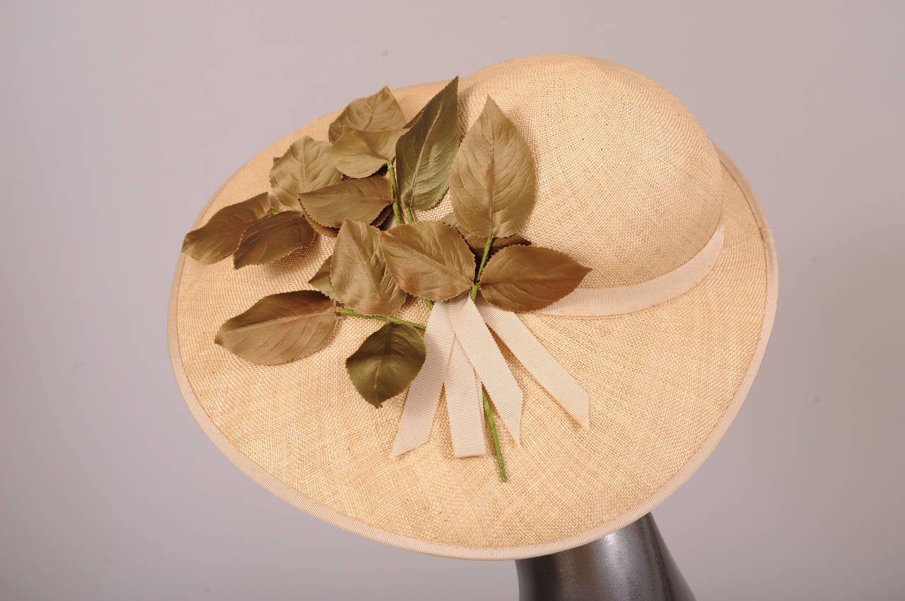 A large brimmed natural straw hat from the 1930's is trimmed with a matching grosgrain ribbon hat band and a large spray of green silk leaves. The hat is in pristine condition.
Measurements;
Width 15.5