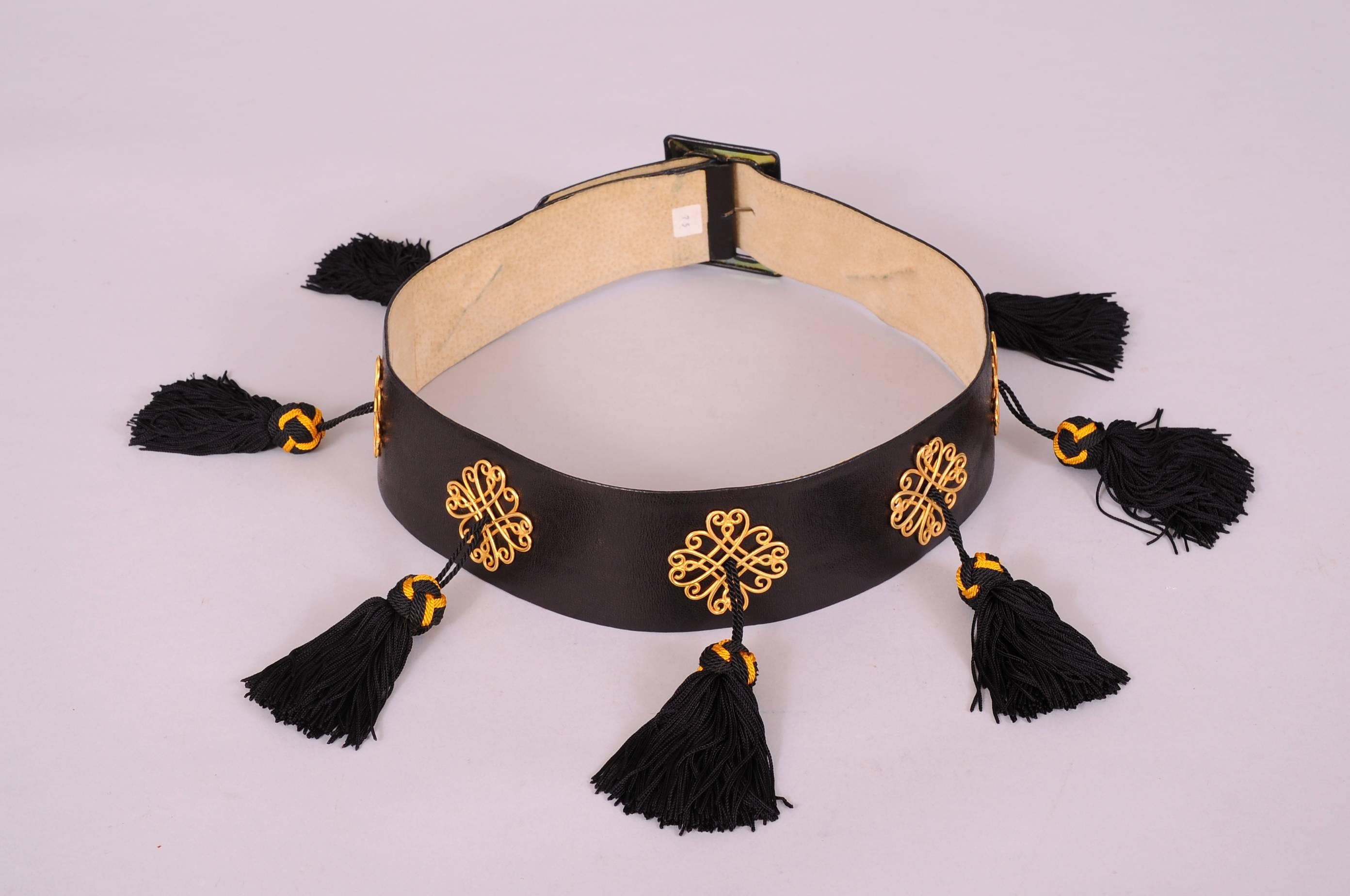 A classic wide black leather belt, curved to fit the waistline, is beautifully embellished by Isabel Canovas. The belt has a leather covered buckle and seven gold toned scrolling medallions. Each of these medallions suspends a black and gold topped