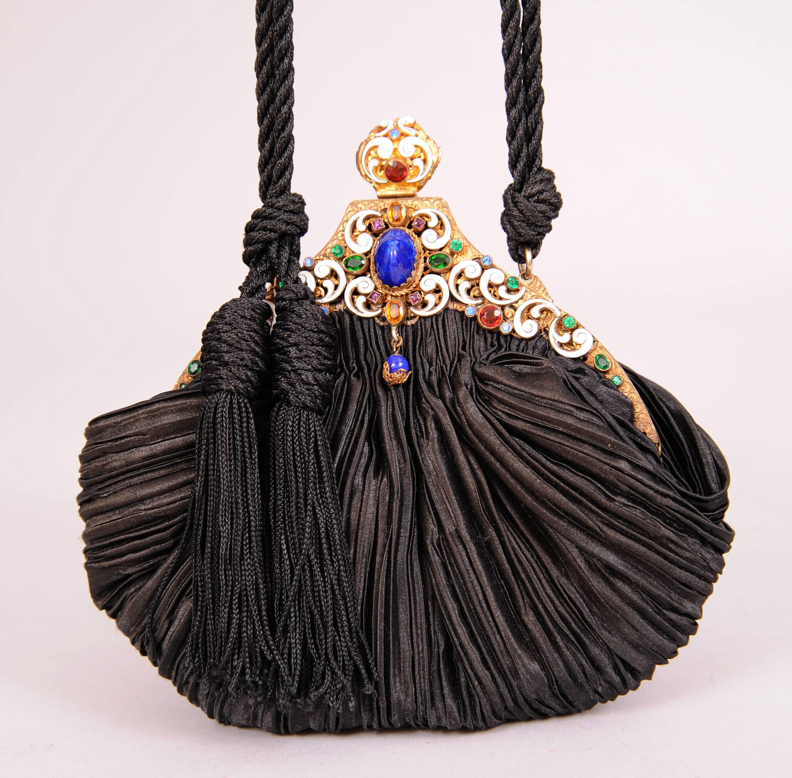 This elegant jewel frame dates to the 1930's and it is set with a large lapis stone at the center surrounded by a white enamel frame and multi color faceted stones. The body of the bag dates from the 1980's and it is black pleated silk. There is a