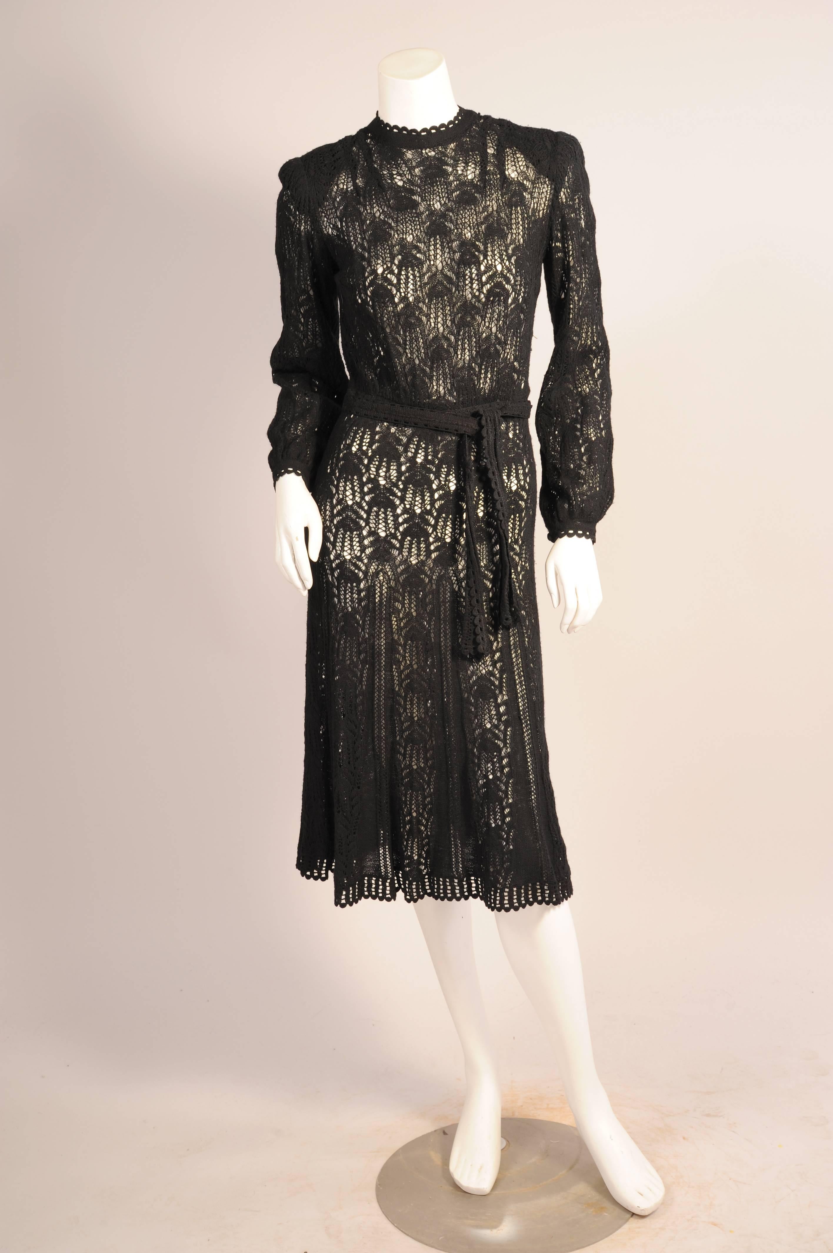 A gorgeous lacey pattern hand knit with fine black wool yarn adds a hint of sexiness to this dress. The round neckline, cuffs, hemline and belt are finished with an open work scalloped pattern. The dress has nine small knit covered buttons at the