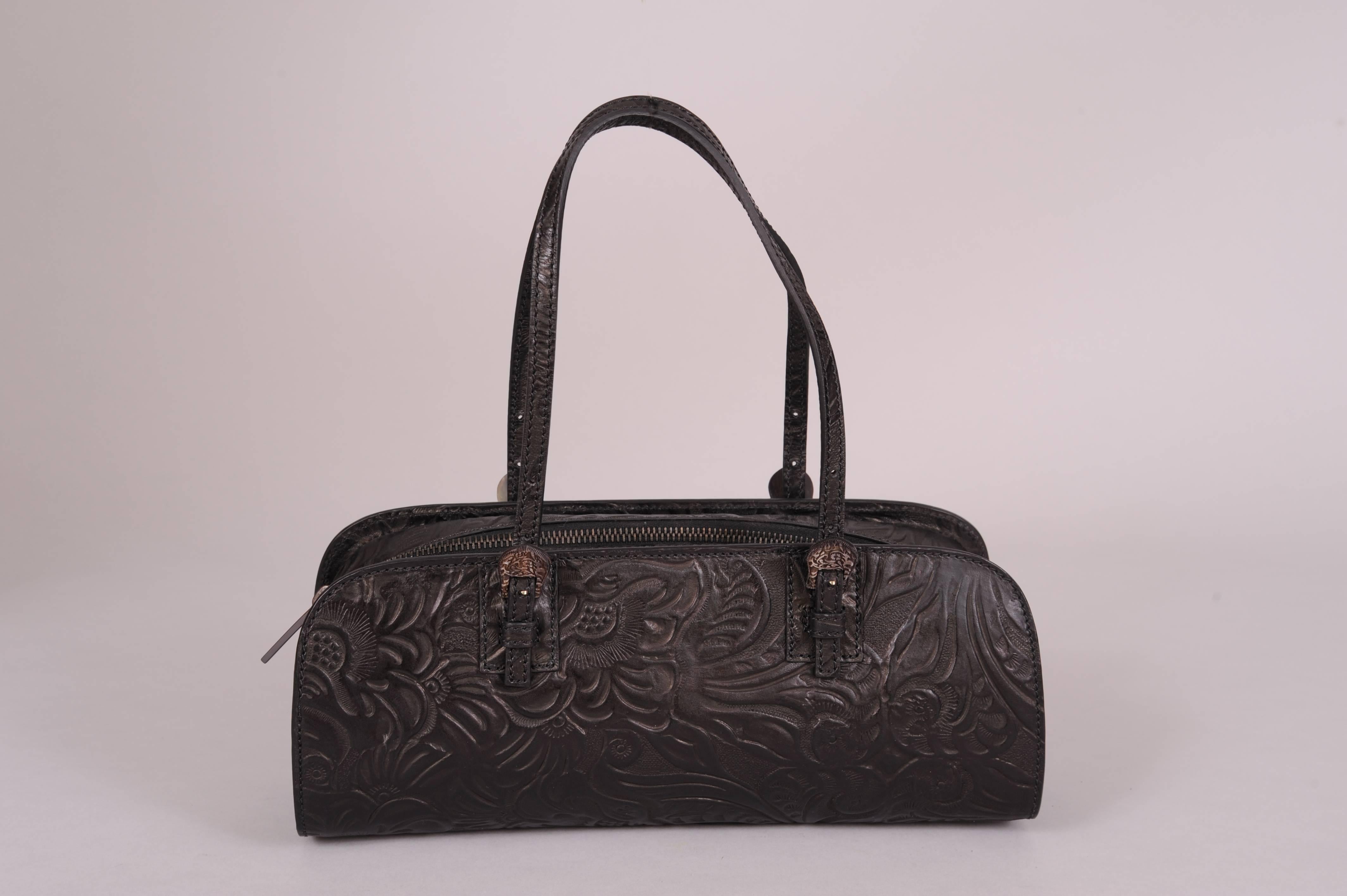 This chic handbag has double straps with dark grey mother of pearl buckles that are carved to resemble Western silver buckles. The bag is tooled leather in a floral pattern with a center top zipper. It is lined in red satin with a zippered pocket