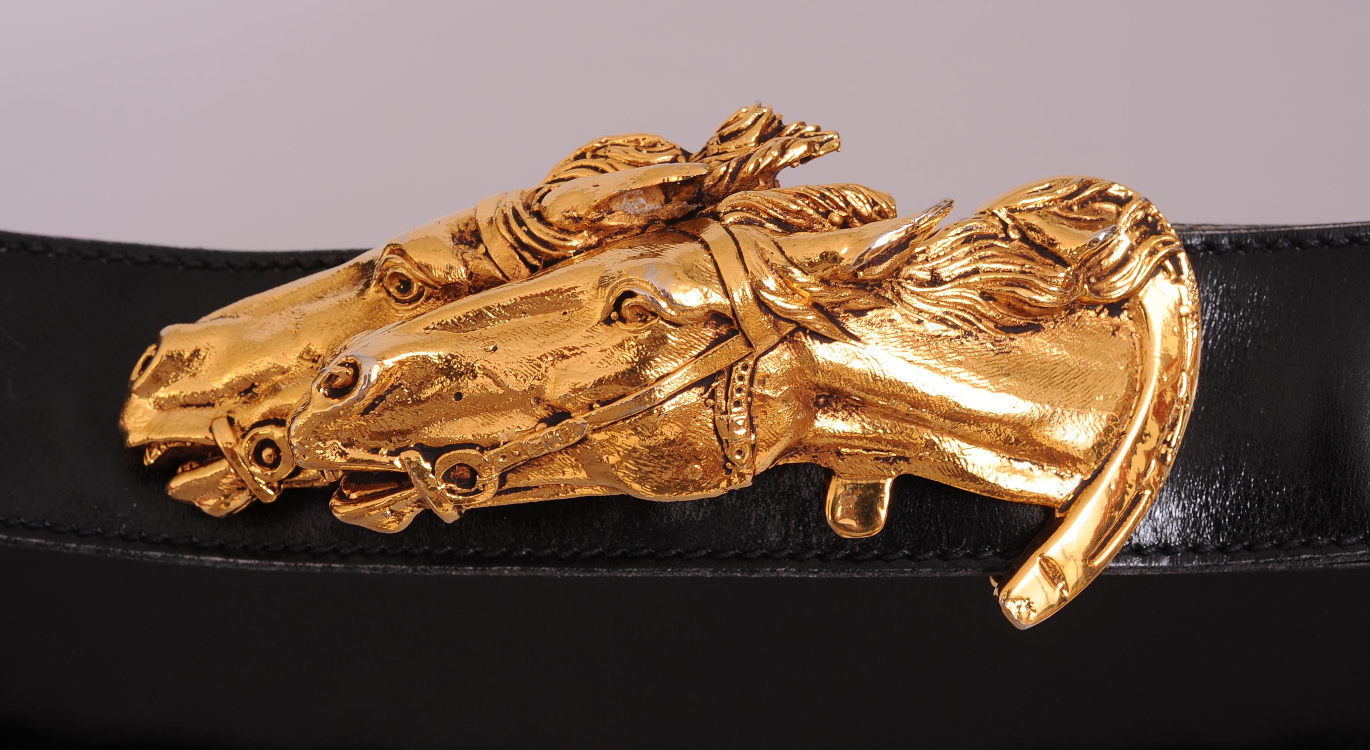 A sculptural gold toned double horse head buckle is further embellished with a horse shoe around one of the animals. It comes with a black leather Gucci belt, stamped in gold, and marked a size 85. Both pieces are in excellent