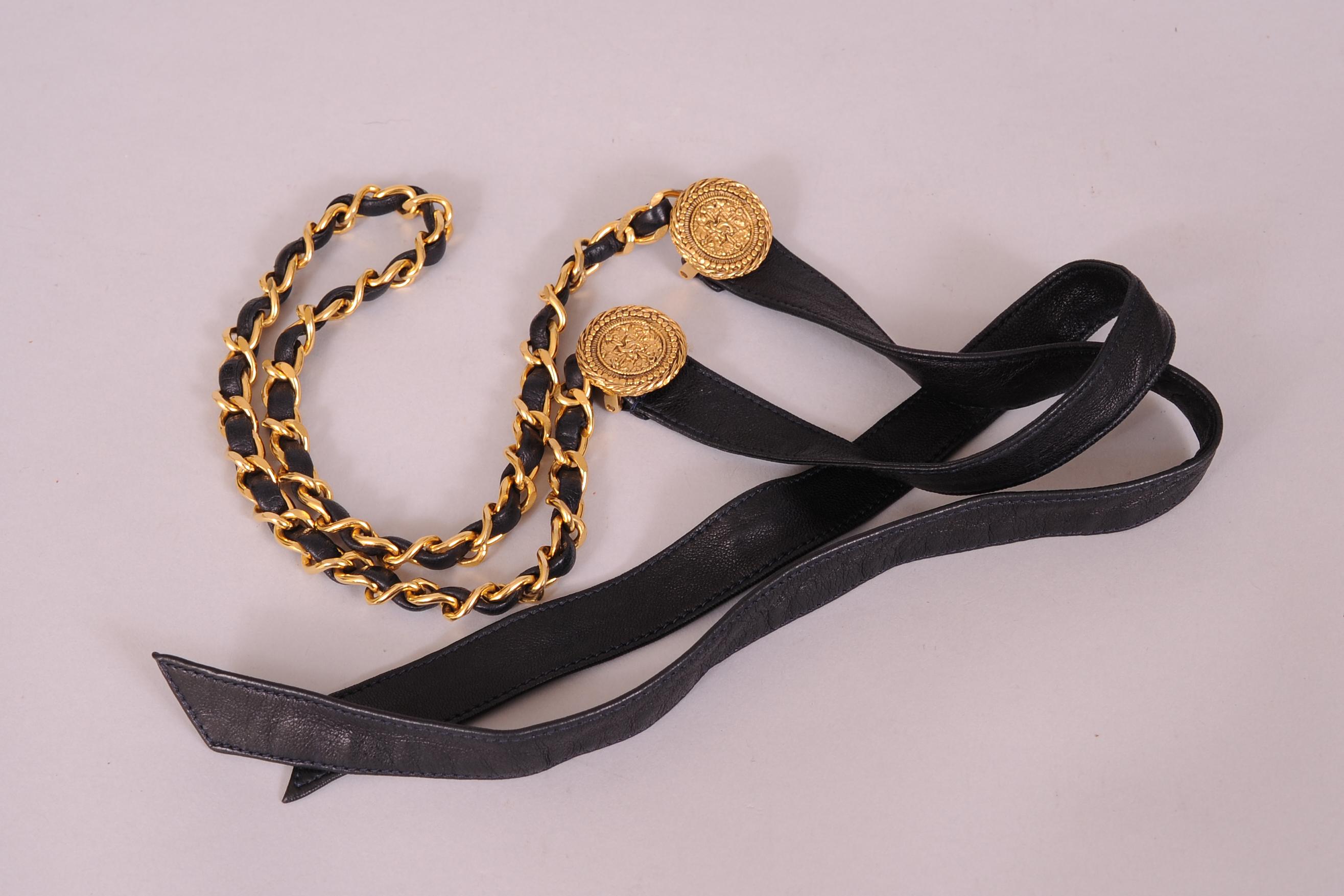 This vintage Chanel belt combines black lambskin leather ties, two logo stamped gold toned medallions, and a center section of the iconic Chanel chain threaded with black leather. It is in excellent vintage condition and is stamped CHANEL Made in