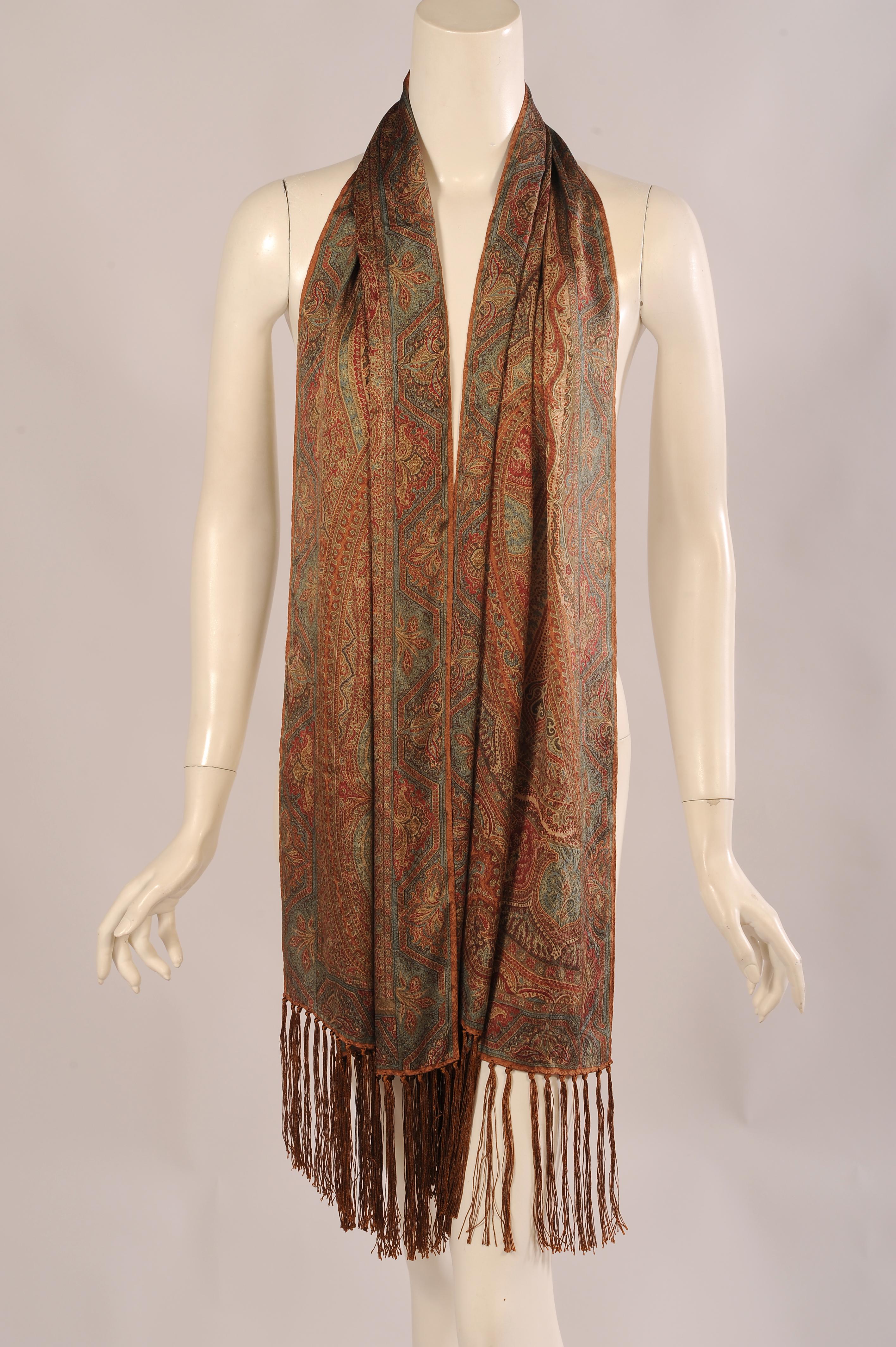 A subtle palette is used for this paisley patterned silk shawl in muted shades of rust, brown, cream, red and blue. The rectangular scarf has brown silk fringe at each end. It is in excellent condition and comes with the original