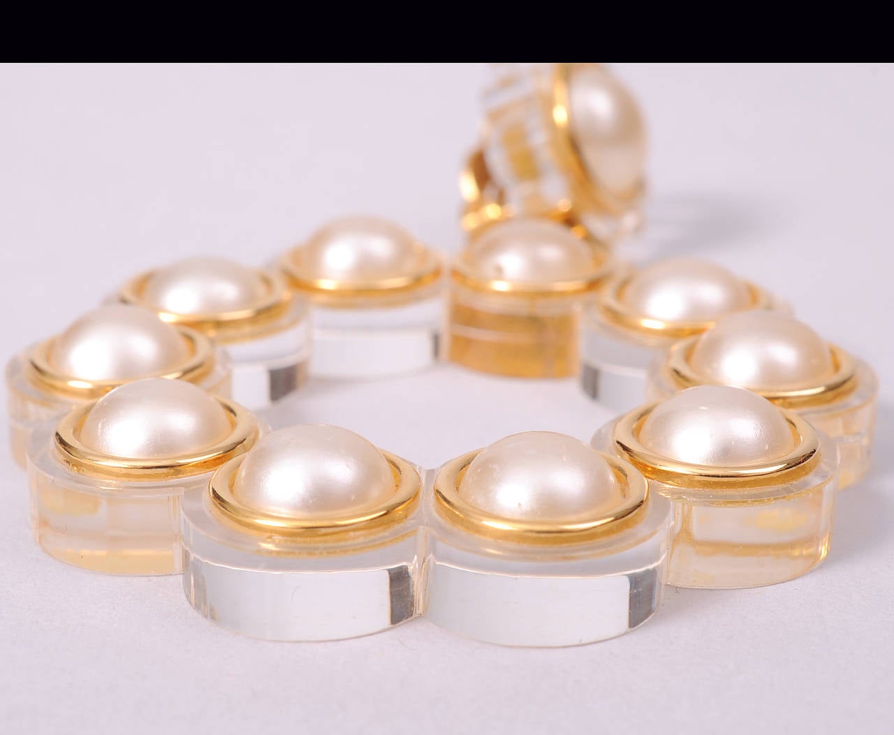 These oversized 1970's inspired runway worn Lucite earrings have a carved Lucite flower centered by a pearl at the top and a scalloped Lucite hoop with 10 matching pearls centered on each curve. All of the pearls are surrounded by gold toned metal