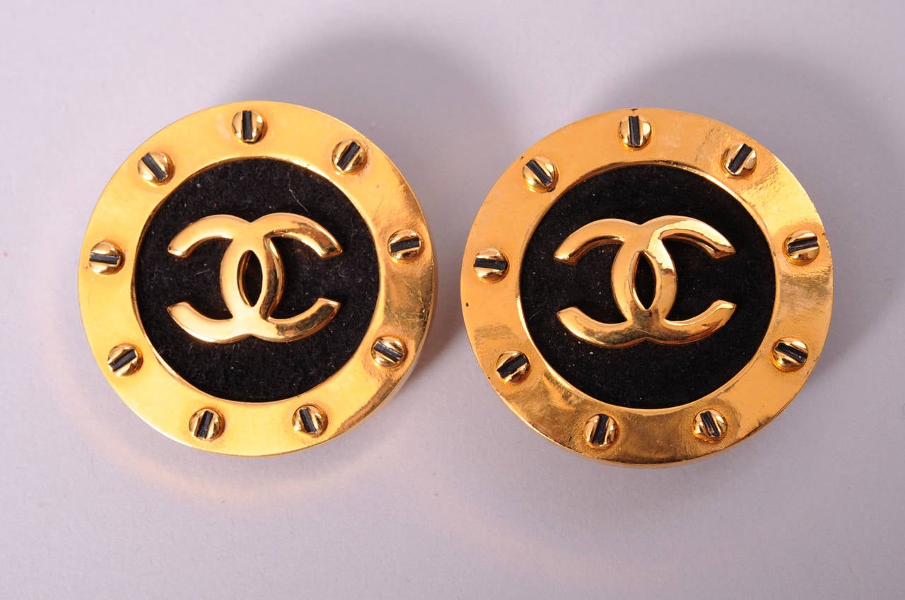 These large Chanel logo earrings were worn once on the runway. The black leather center has the double C logo in gold toned metal. The edge is trimmed with gold dots resembling faux screw heads. The earrings are clip on and they are in excellent