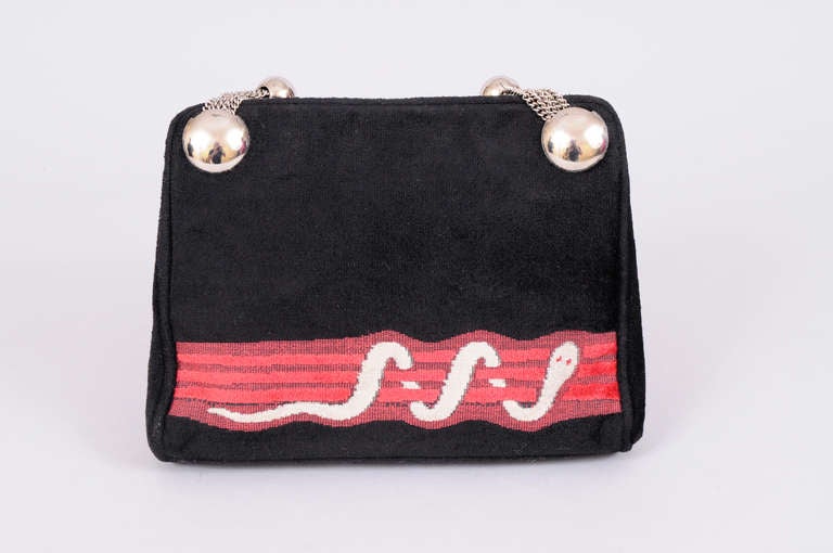 Black velveteen is accented with a red woven velveteen band showcasing a cream velveteen snake with red eyes. The bag has a fabulous silver toned ball and chain strap and a silver toned push closure. It is lined  with black leather and has one