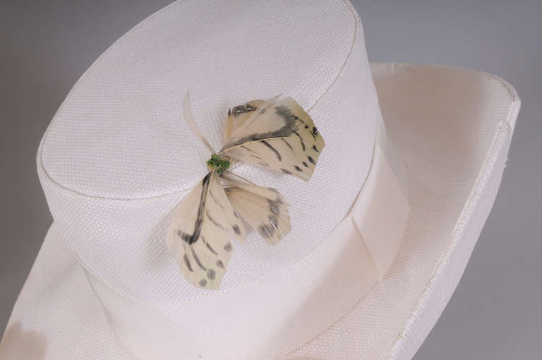This charming woven fabric hat has a turned up brim on one side. It is trimmed with a wide gros grain ribbon and four feather butterflies. The exterior is in excellent condition. There is a slight discoloration on the front of the interior hat