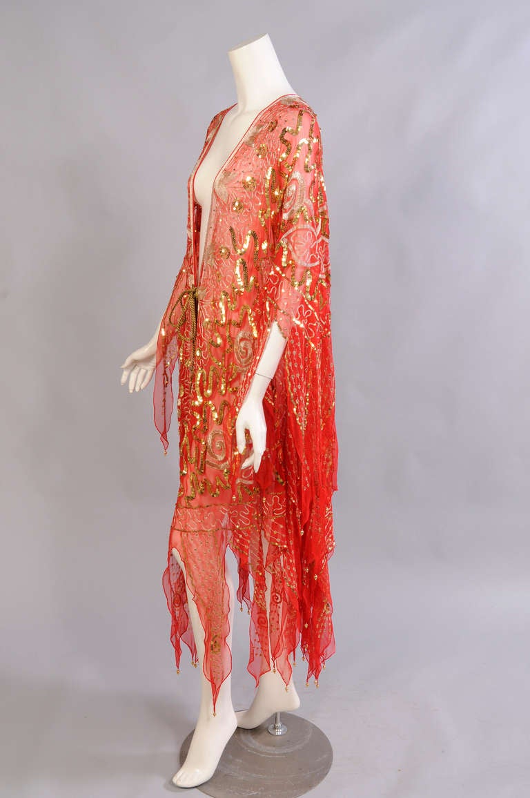 Brilliant orange silk chiffon is lavishly embellished with a pattern worked in gold embroidery and sequins. Gold beads accent the tip of each separate panel on the sleeves and the hem. There is a gold metallic cord closure at the center front. This