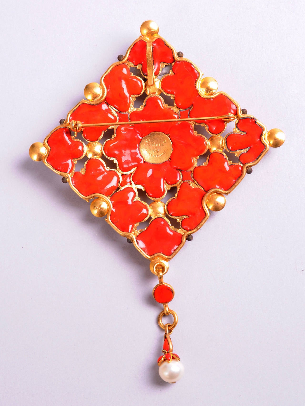 A striking diamond shaped pin or pendant in delicate gold filigree is backed with bright orange poured glass which peeks through the gold work. Pearls and orange cabochon poured glass stones add further interest. This piece is in excellent