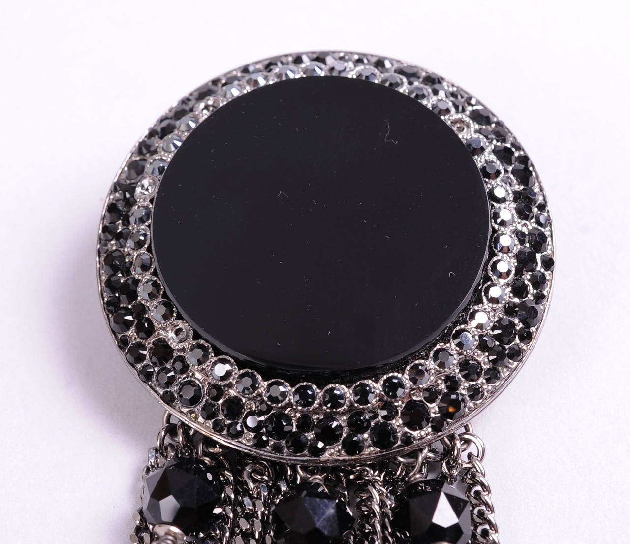 An elegant and modern look from Chanel, this brooch has a large black Gripoix center stone surrounded by rows of black faceted beads set in silver toned metal. A fringe of silver toned chains and black beads dangles from the bottom. This piece  is