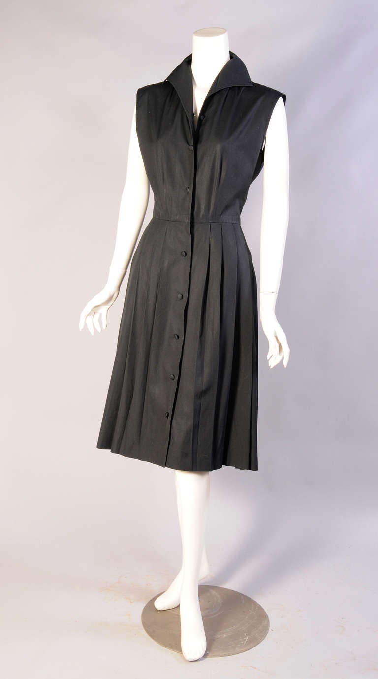 Classically elegant, this black cotton sleeveless dress is a shirtwaist style from Emilio Pucci with a pleated skirt. It buttons at the center front with matching fabric covered buttons and it is in excellent condition. The dress is marked a vintage