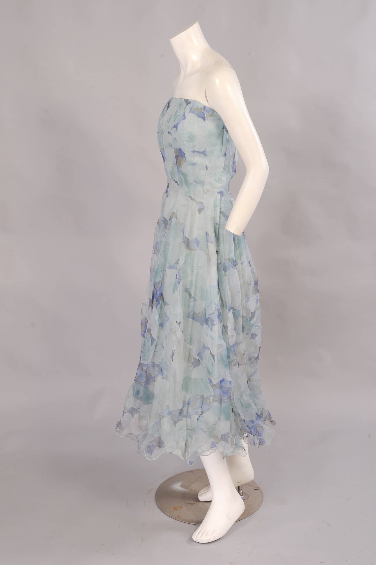 This Spanish made, pale blue water color floral print silk organza dress has a fitted and boned bodice. The gored skirt is seamed for added fullness and finished with a flounce at the hemline. The dress is fully lined in pale blue cotton and there
