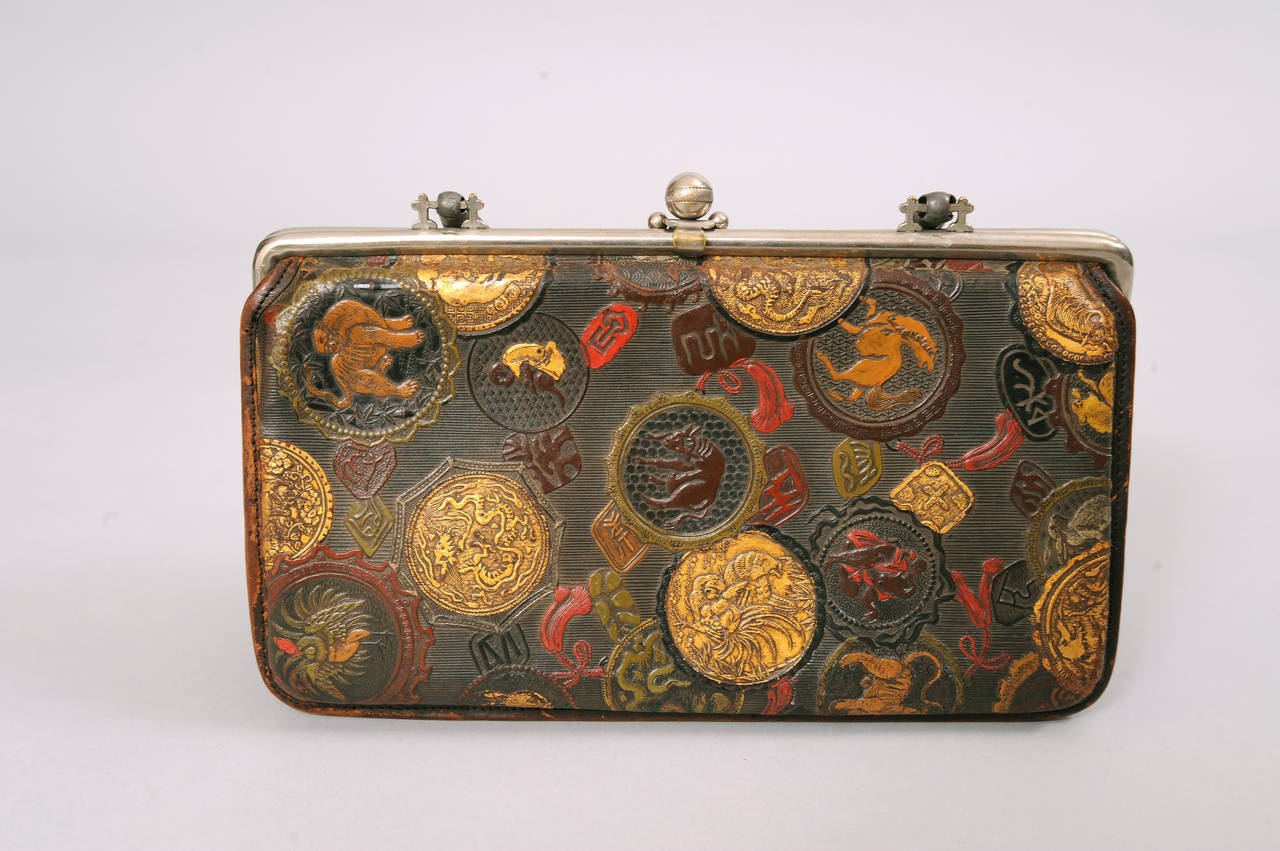 This deep brown leather bag is covered with auspicious Chinese symbols in red, camel, olive green and shimmering gold. The bag has a small pocket on the front with a clasp that is marked LM & Co. and dated March 12, 1878. The bag has a metal frame
