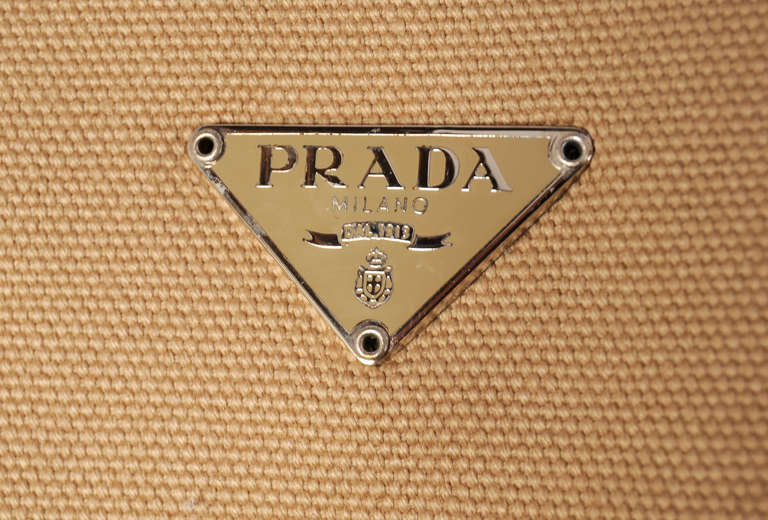 Tan canvas is trimmed with lime green leather corners and straps on this tote bag from Prada. The bag has a magnetic clasp above a zippered interior pocket. It bears the Prada logo on the outside. Never used, it is in excellent