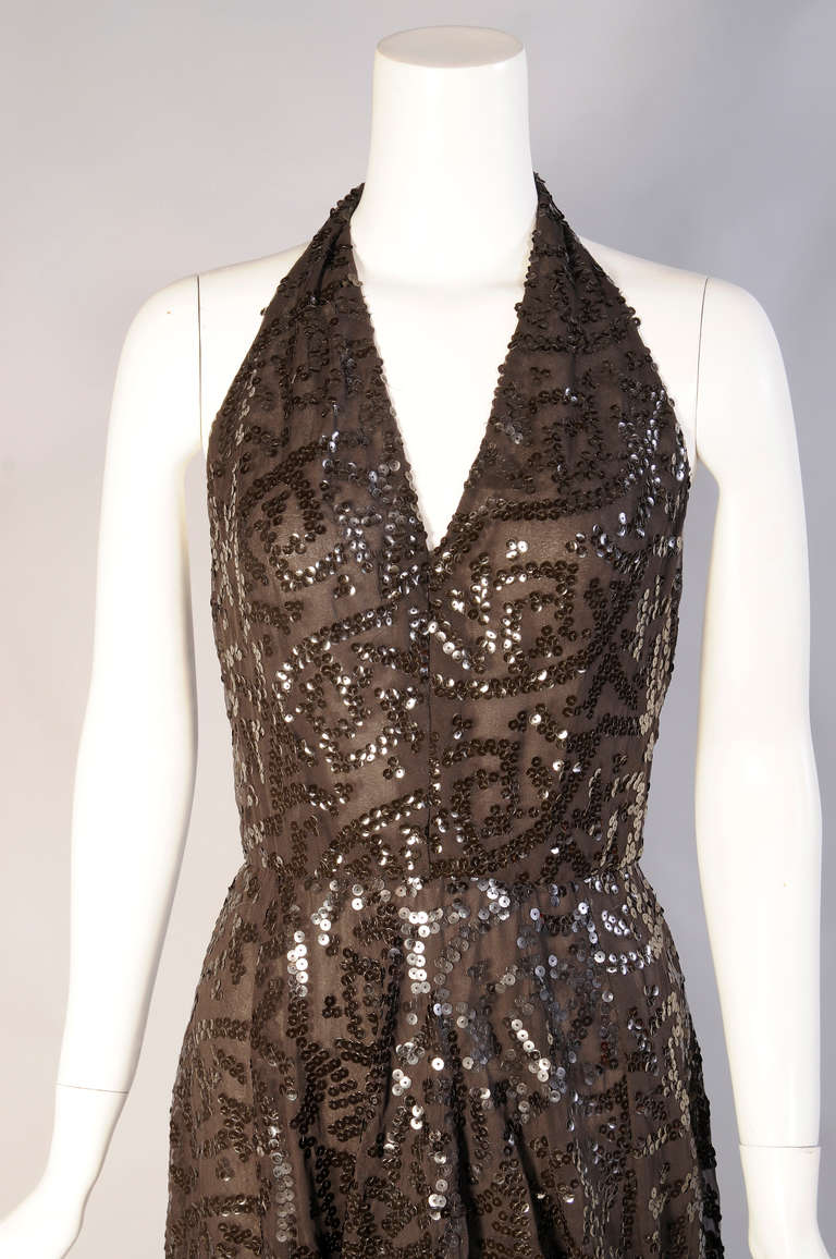 A plunging halter neckline and low cut back bring a sexy glamour to this sequin covered chiffon dress. The gown has a fitted waist and center back zipper. The sequins are applied in a vermicelli pattern on chiffon. Two more layers of chiffon add