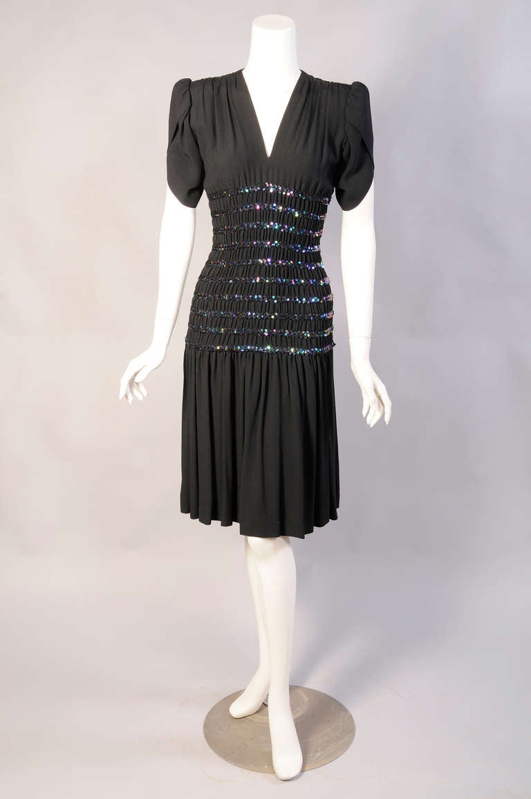 Yves Saint Laurent takes his inspiration from the 1940's for this great black crepe dress with a beaded and gathered design. The dress has a V neckline and tulip sleeves. It slips on over your head with an elasticized mid section. The carnival