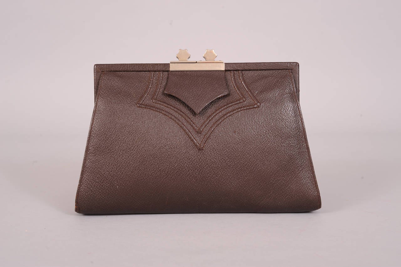 Textured dark brown leather has  a raised detail on the front echoing the leather tab. A vertical leather handle is on the back. Two chrome stars top the clasp. There is an open pocket with the original mirror and a kiss lock divider in the center