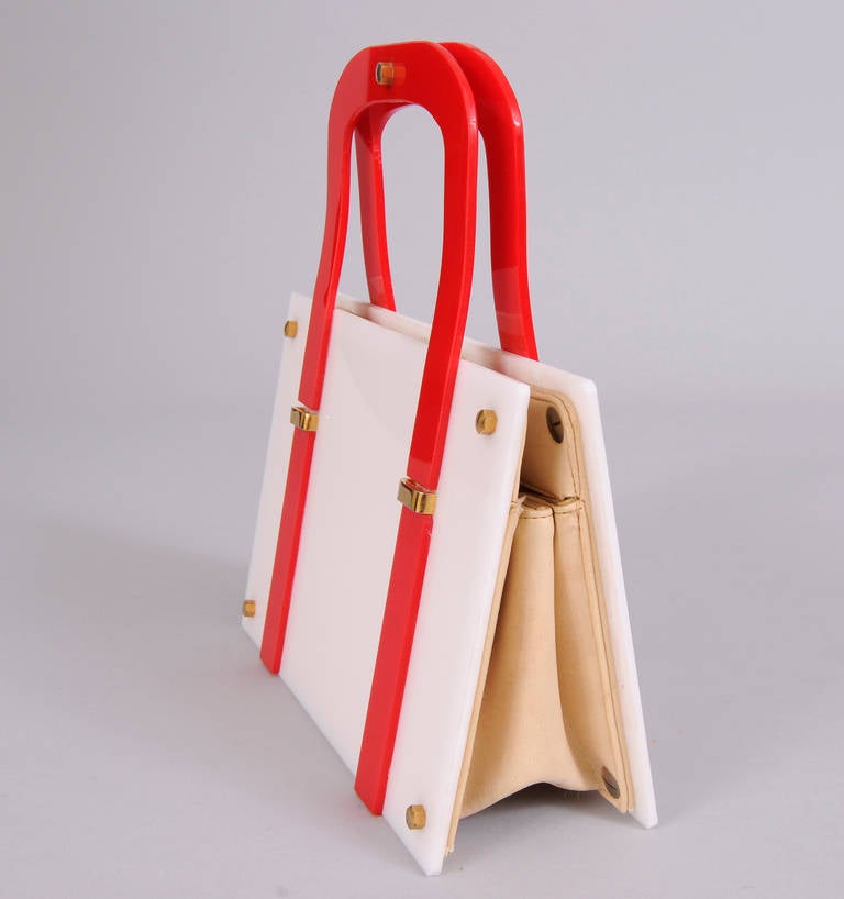 A striking red and white Lucite bag from the 1970's is trimmed with gold toned hardware. The bag has a beige man made lining with one slip pocket. It is in excellent condition.