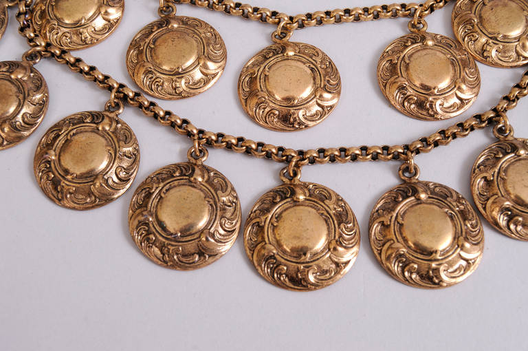 A double row of gold toned discs with a sculpted design create a glamorous bib necklace from YSL. The necklace has never been worn and still retains the original YSL tag. It is in excellent condition.