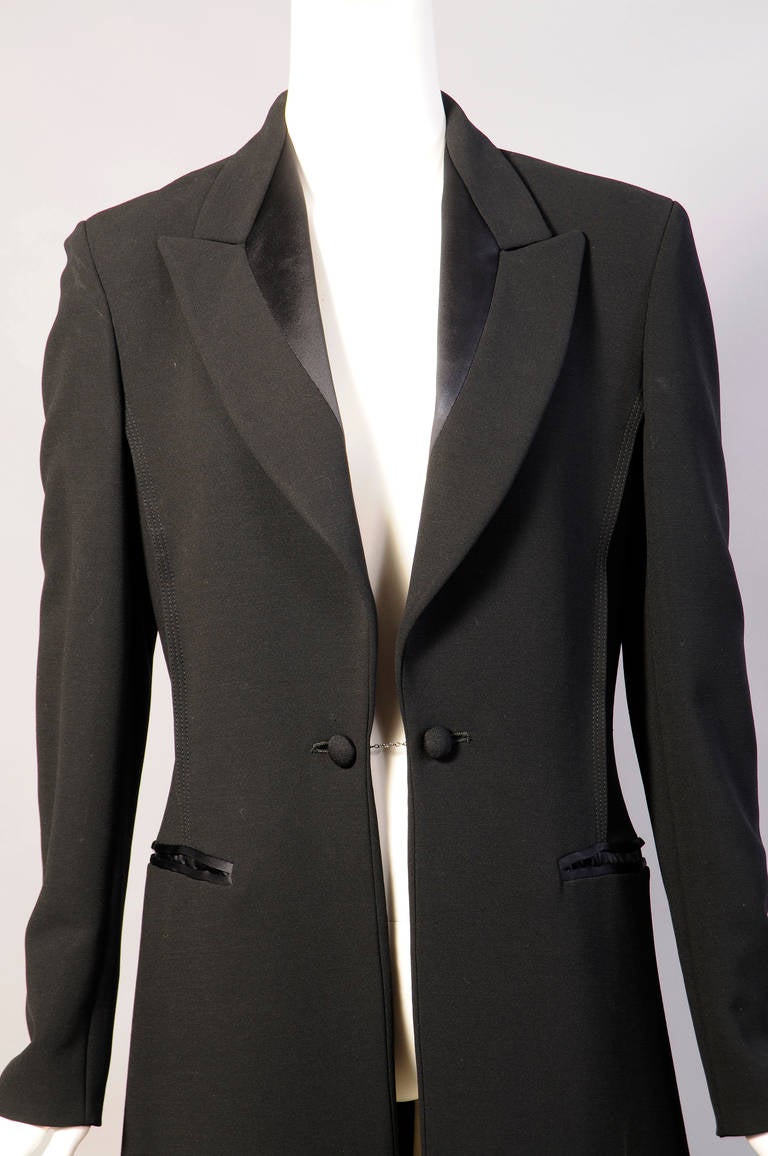 A classic tuxedo jacket or tail coat is the inspiration for this elegant long coat made from fine black wool with black satin lapels and cuffs. The coat has two large buttons on a chain at the center front and cufflinks on the satin French cuffs.