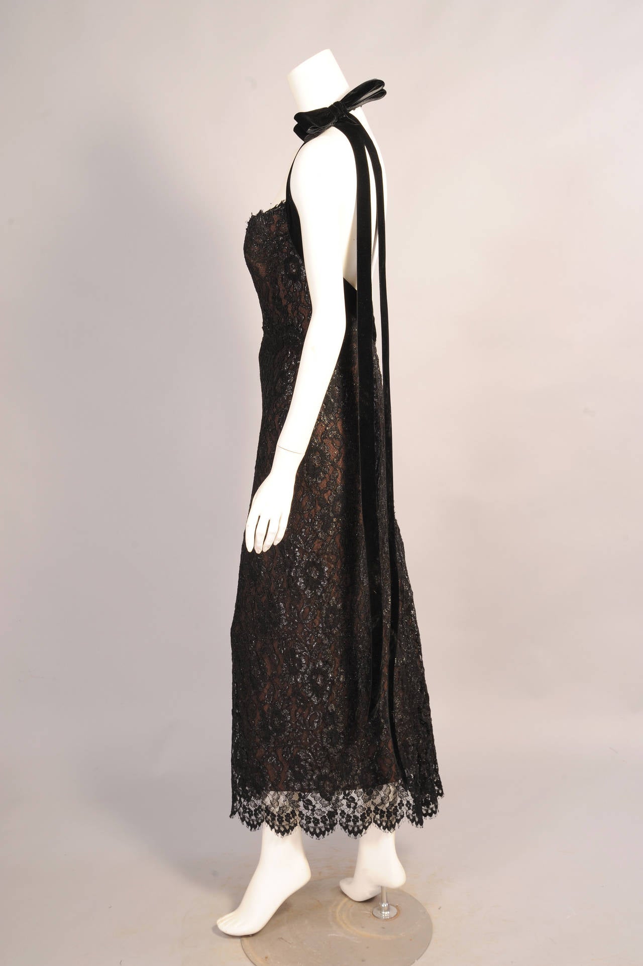 Glistening black lace over black chiffon over nude chiffon creates a subtle and striking contrast on this sexy halter dress from Bob Mackie. The bodice is fully boned and trimmed with a wide black velvet ribbon. The halter hooks at the center back