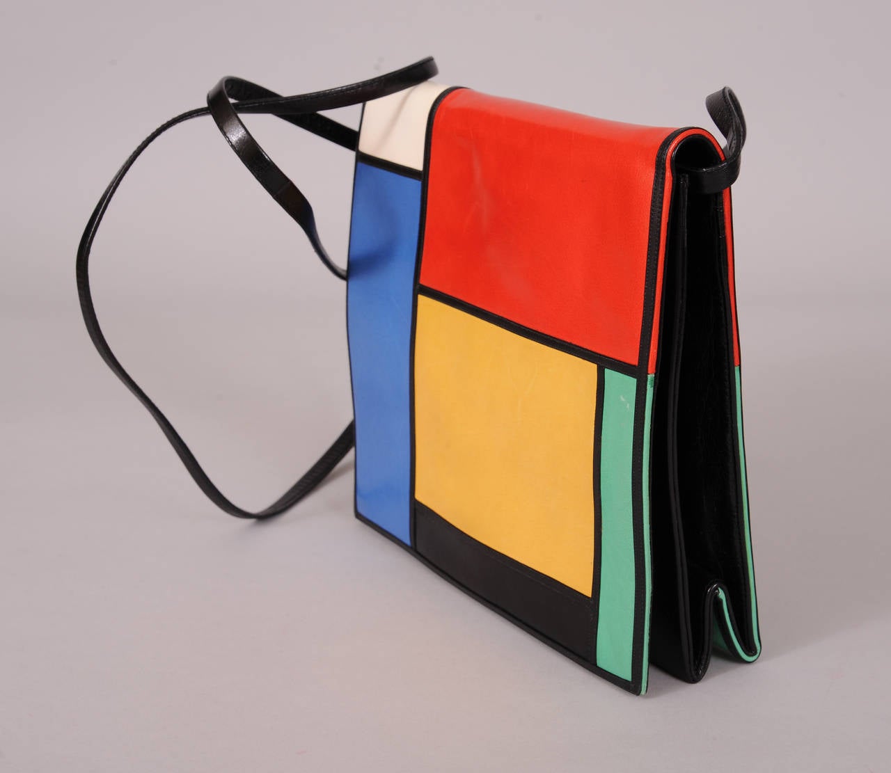 Inspired by the colorful artwork of Mondrian this bag is composed of bright geometric shapes bordered by black leather. The removable shoulder strap and the interior flap are black leather. The body of the bag is beige suede. There is a zippered