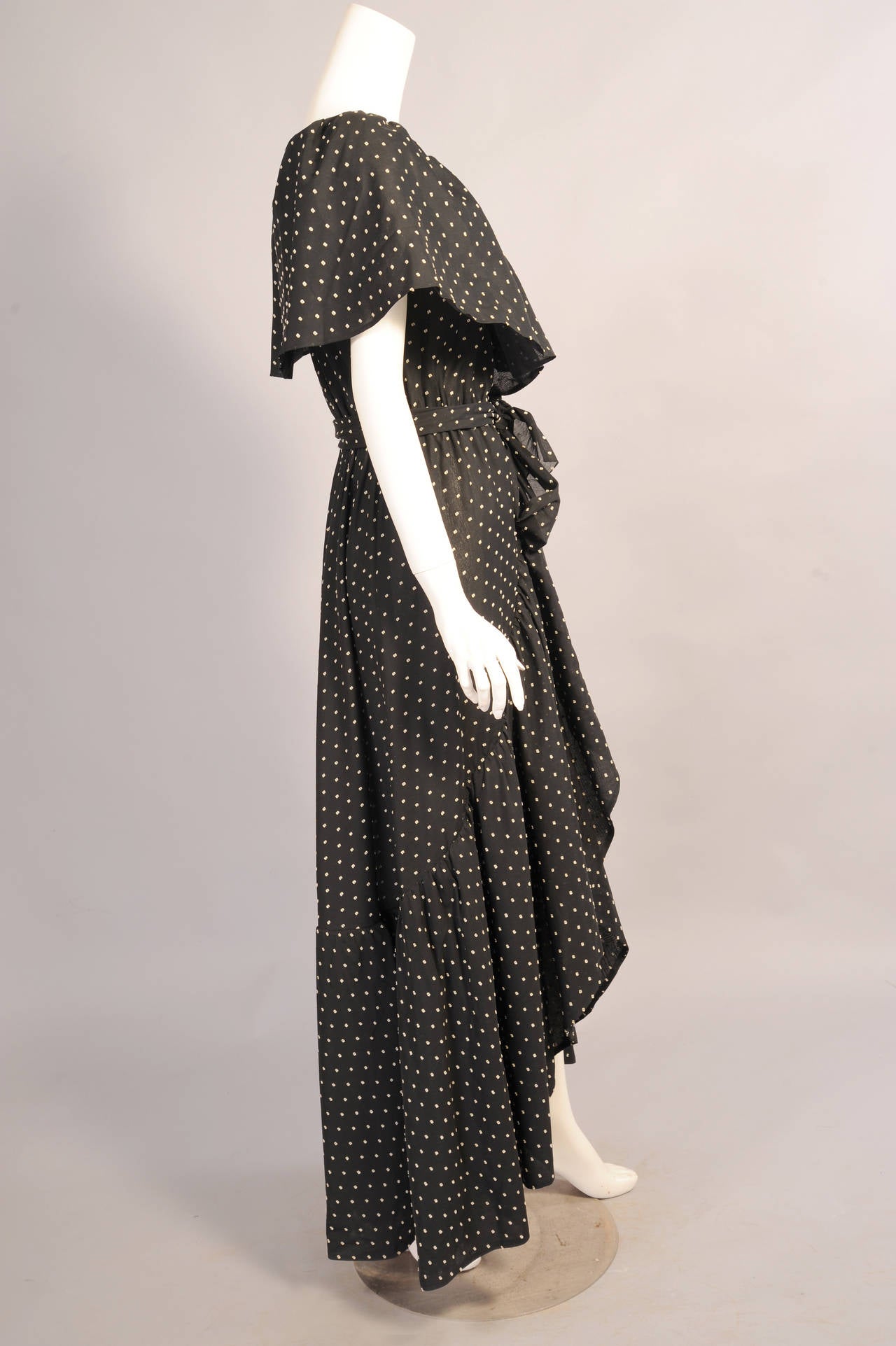 A black cotton with a white Swiss dot is used for this glamorous and sexy dress designed by Halston in the 1970's. A wide ruffle creates a cape look on the bodice of the sleeveless dress. There are hooks and eyes at the elasticized waistline and the
