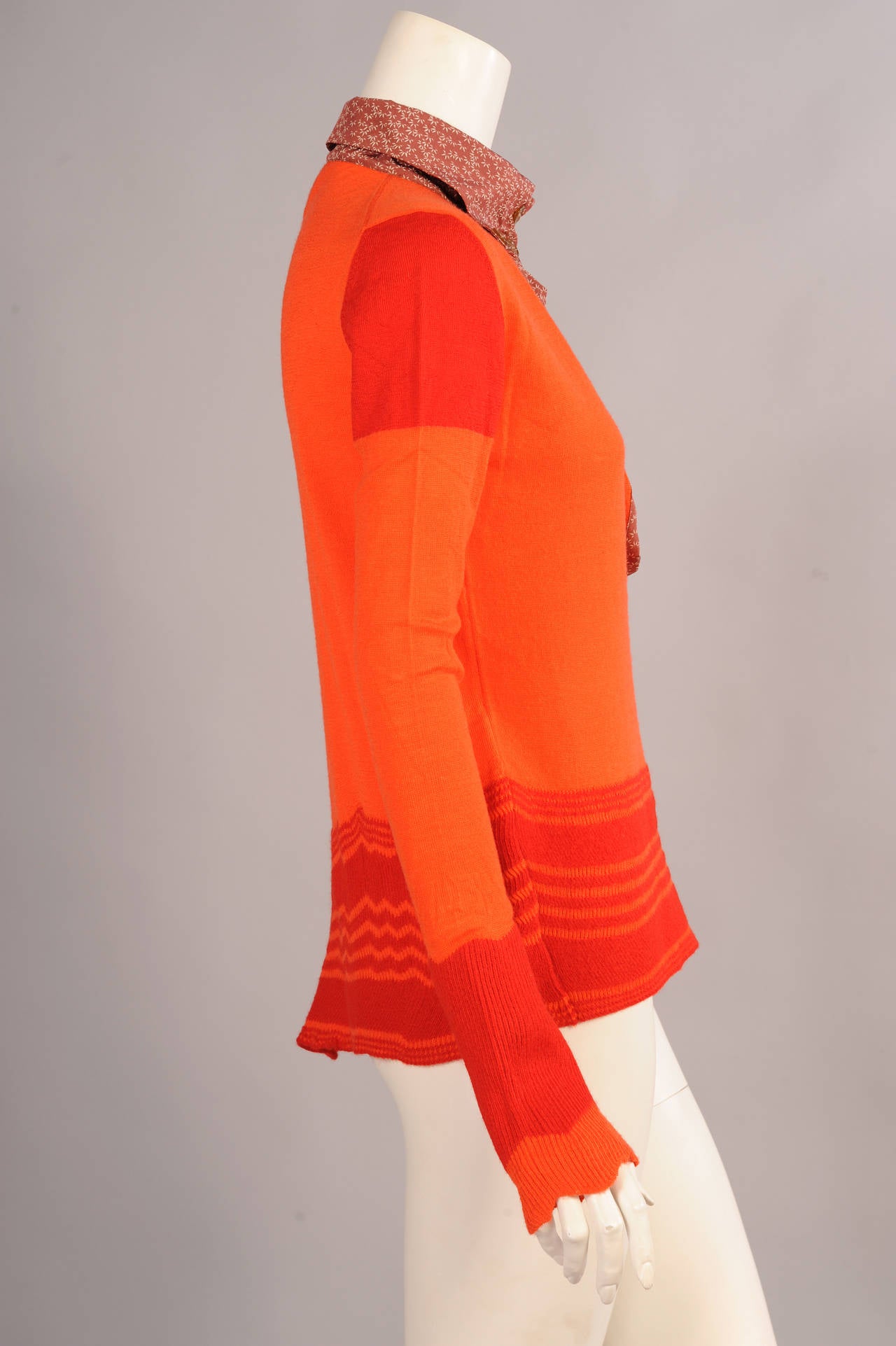 Bright orange wool is accented with bands of red on the sleeves and red and orange on the hemline. The sweater has a printed cotton button down collar with two additional buttons at the neckline. It has never been worn, comes with extra buttons, and