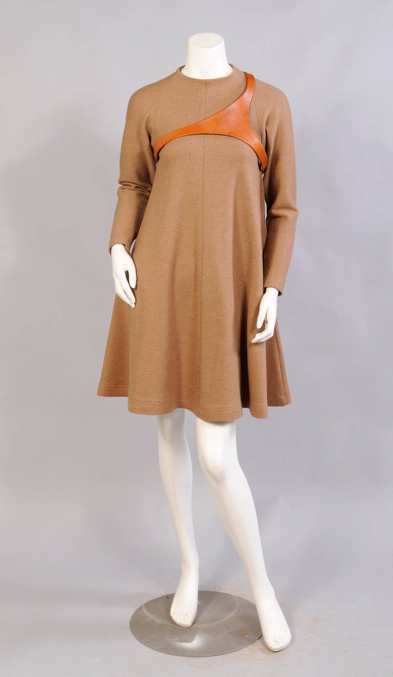 A spare and elegant trapeze dress, made from camel colored wool comes with a caramel leather harness in a signature Geoffrey Beene shape. The dress has small zippers at the wrists and an invisible zipper at the center back. There are pockets