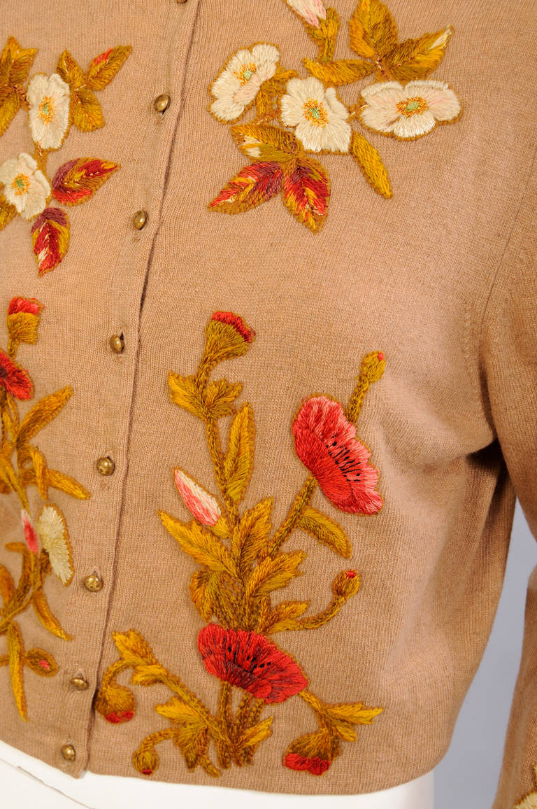 A camel colored cashmere sweater is beautifully hand appliqued with floral motifs. The appliques have been cut from a hand embroidered antique textile and then sewn onto the front, back and sleeves of the sweater. It is lined in cream colored silk