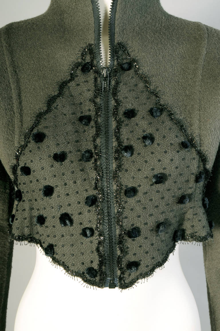 This moss green wool jacket with a zipper closure is decorated with black point d'esprit tulle and plush pom poms on either side of the center front zipper. It is iunlined and bears the Beene label as well as the label of Nan Duskin, an exclusive