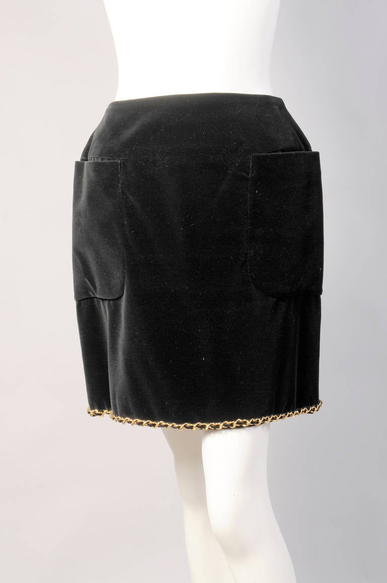 Rich black cotton velvet has a wide band that sits just below the natural waistline. There are two generous patch pockets and the signature gold chain is used on the outside of the hemline. This decorative chain is threaded with a black velvet