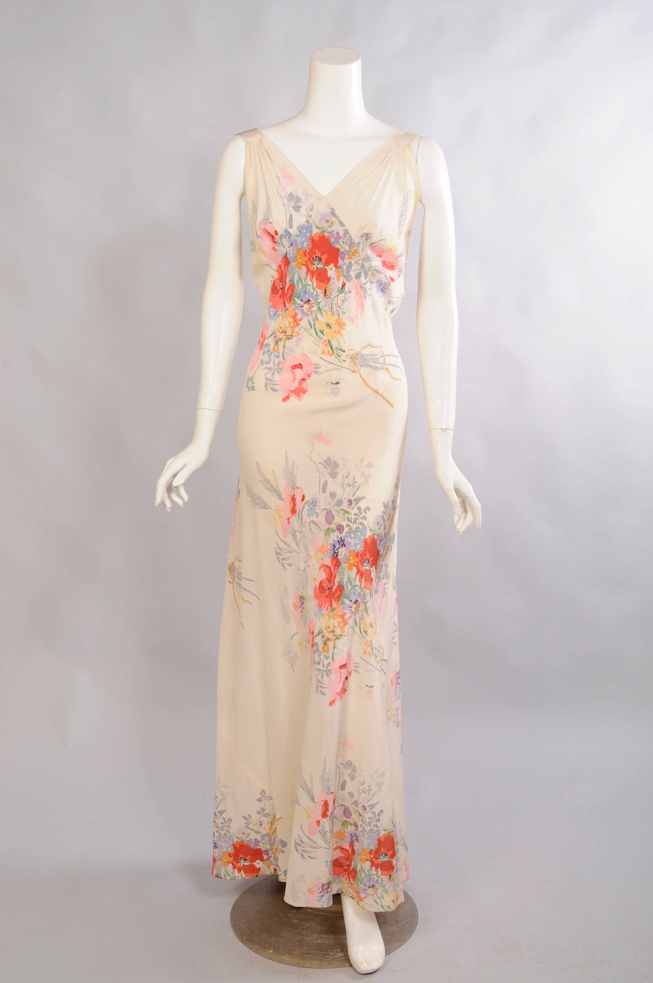 A colorful floral bouquet is set against the ivory silk georgette background for this 1930's bias cut evening dress.  There is a V neckline which dips low in back with wide straps. The dress has a slight train and it closes with hooks and eyes. A