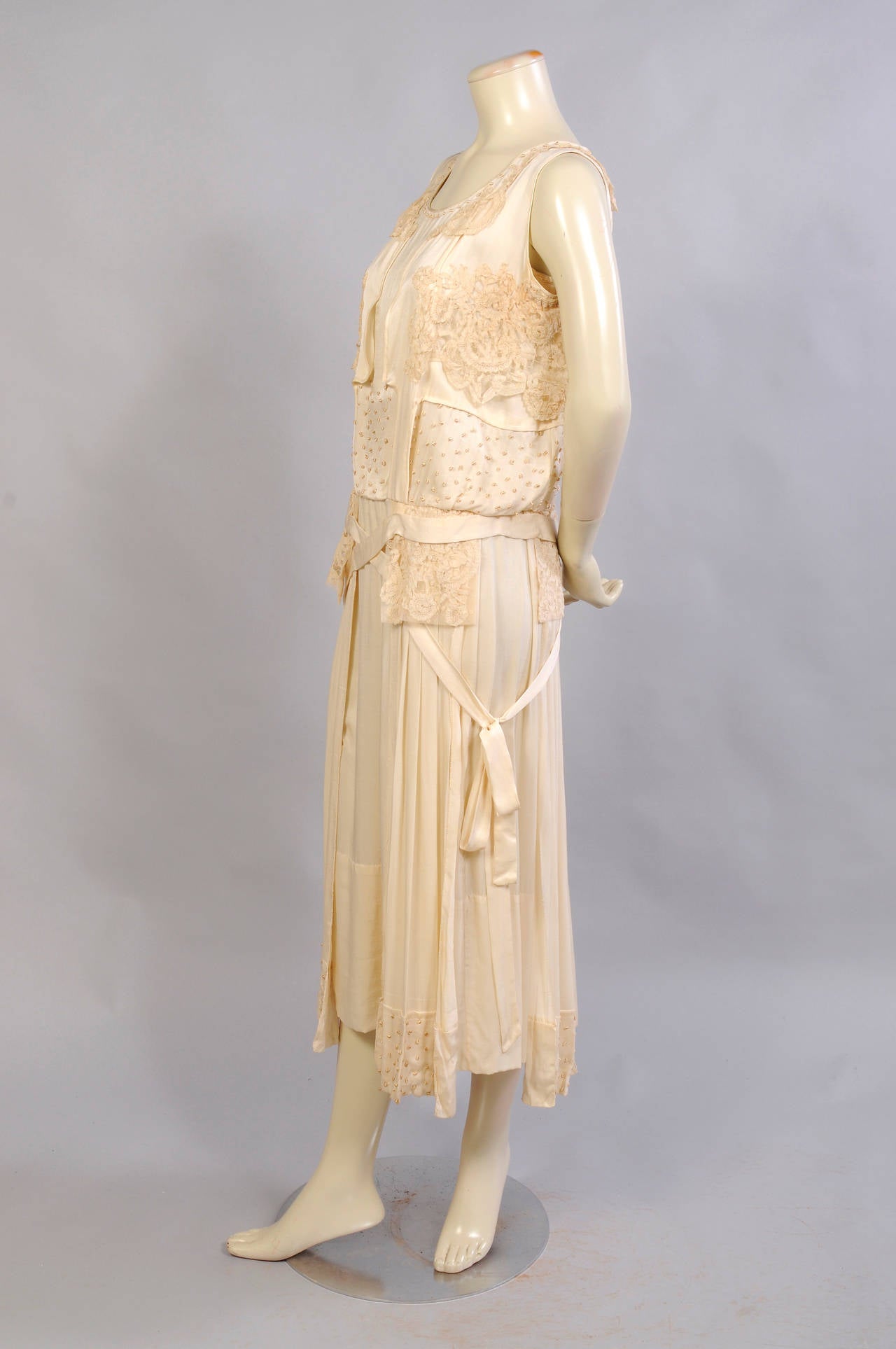 This 1920's silk dress has so many interesting design elements. There are silk French knots at the neckline as well as tape lace panels.
Rows of French knots are sewn above the waistline and more lace sits atop the pleated panels on the hips. These