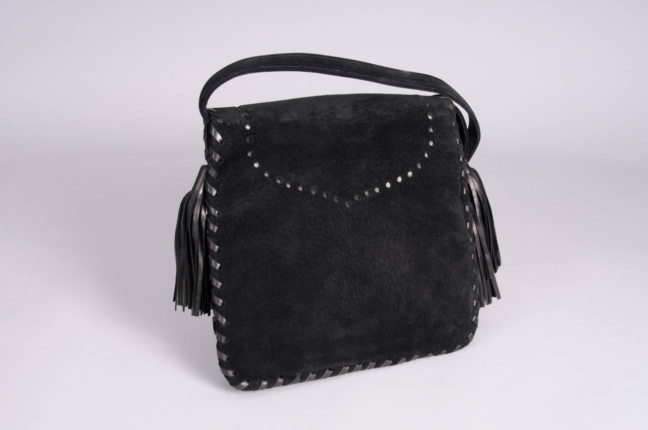 Black suede is trimmed with black leather lacing and tassels to create a chic bag from YSL. There is an open pocket under the flap and two interior sections, with one zippered pocket. The bag is in excellent condition.
Measurements;
Height