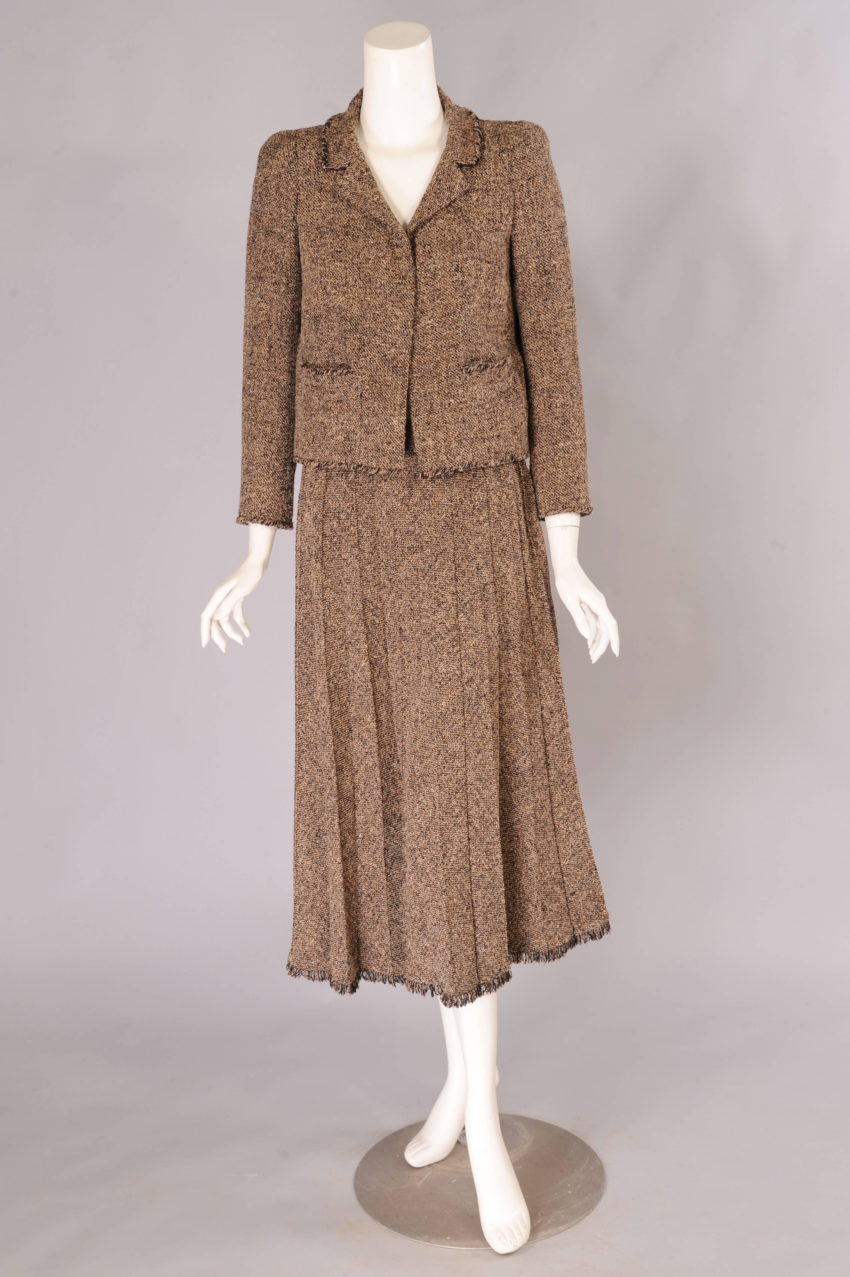 This beautiful tweed suit in shades of black and beige with a hint of coral has the classic Chanel braid trim on the collar, cuffs, pockets and hemline. The jacket is fully lined in hand finished black silk and it has the gold chain on the inside