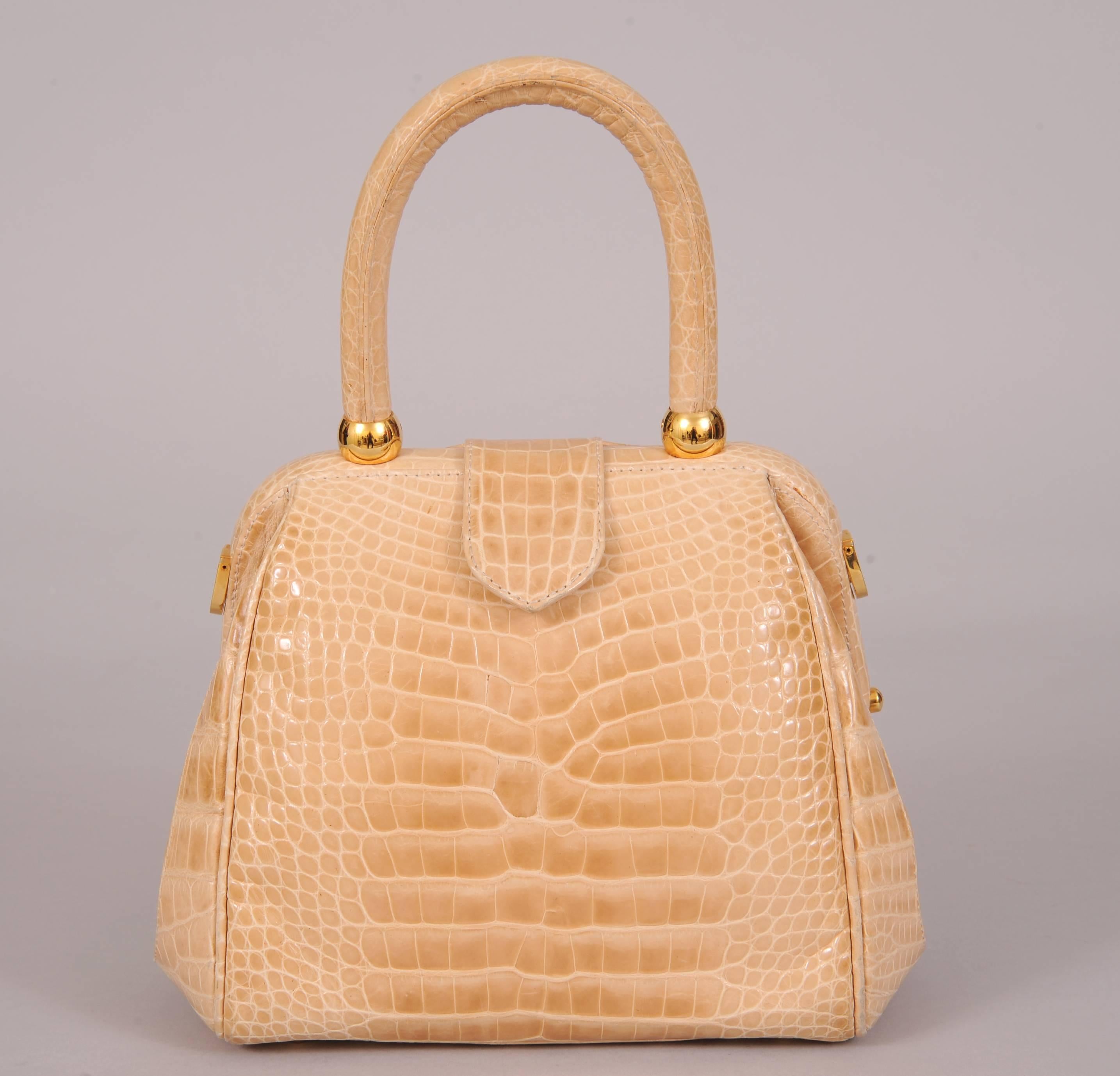 A warm cream colored alligator bag from Lana Marks has a generous pocket on the front. The snap closure tab reaches over the frame to close on the back. The bag is lined in cream leather and has one zippered pocket and one slip pocket inside. An